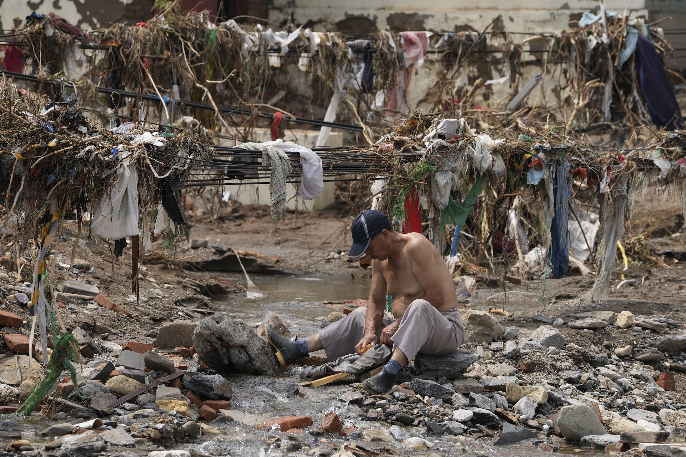 A man washes his clothes in a stream near debris left over after flood waters devastated the village of Nanxinfang on the outskirts of Beijing