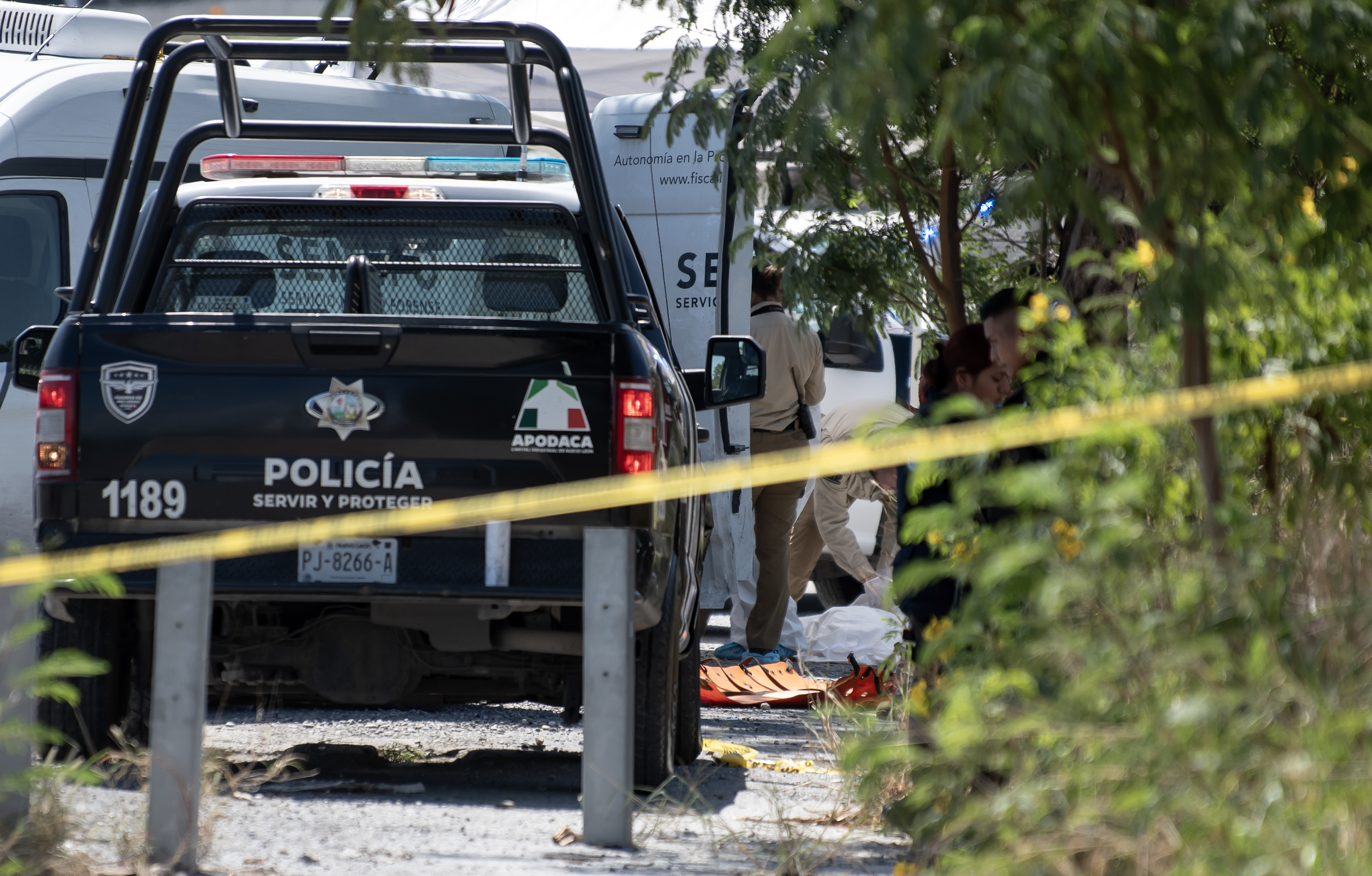 A yellow police tape with a police truck behind it and forensic experts at work.