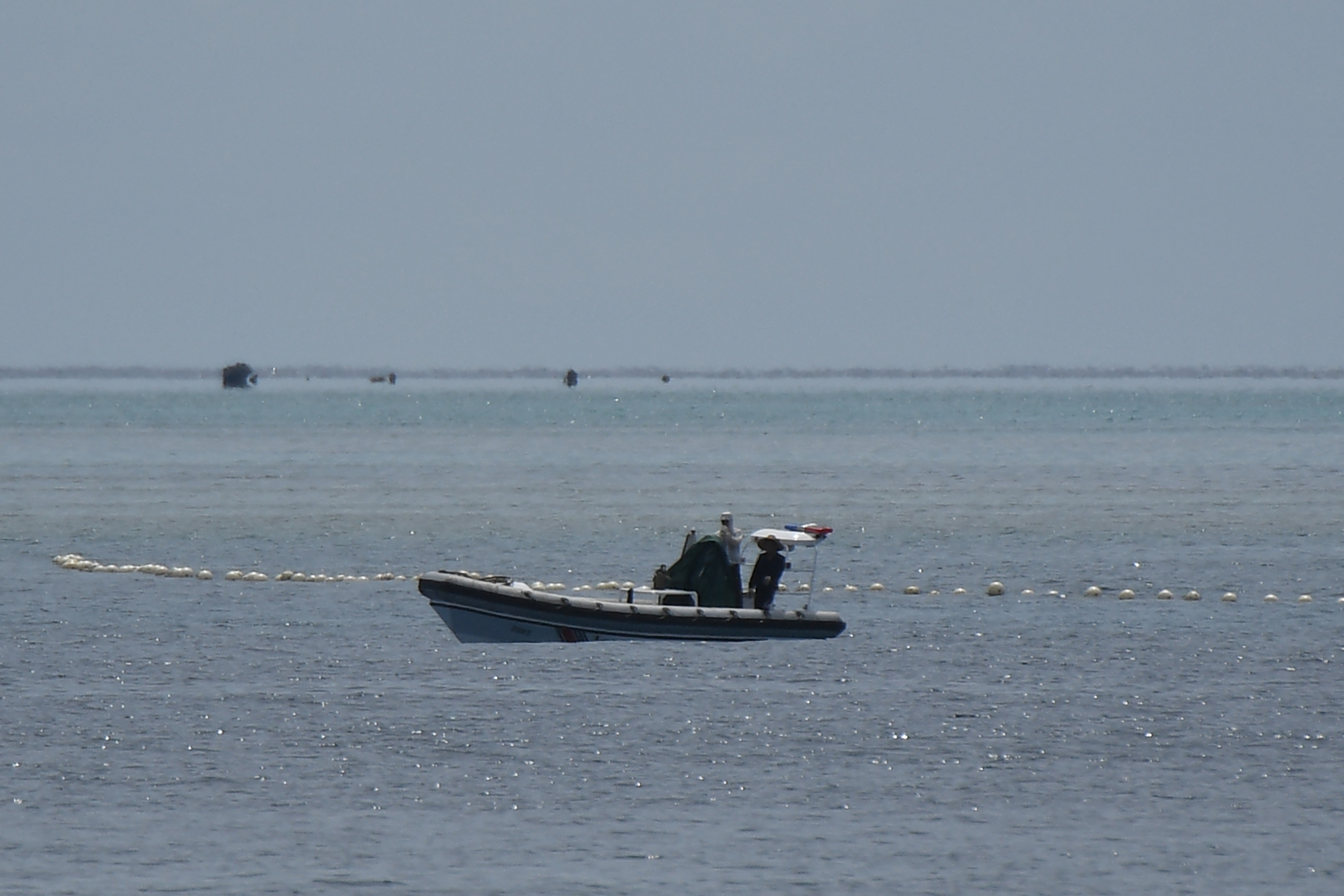 This photo taken on September 22, 2023 shows Chinese coast guard personnel aboard their rigid hull inflatable boat beside a floating barrier as they guard a passage to the Chinese-controlled Scarborough Shoal in disputed waters of the South China Sea. China, which claims sovereignty over almost the entire South China Sea, snatched control of Scarborough Shoal from the Philippines in 2012. Since then, it has deployed coast guard and other vessels to block or restrict access to the fishing ground that has been tapped by generations of Filipinos. (Photo by Ted ALJIBE / AFP)