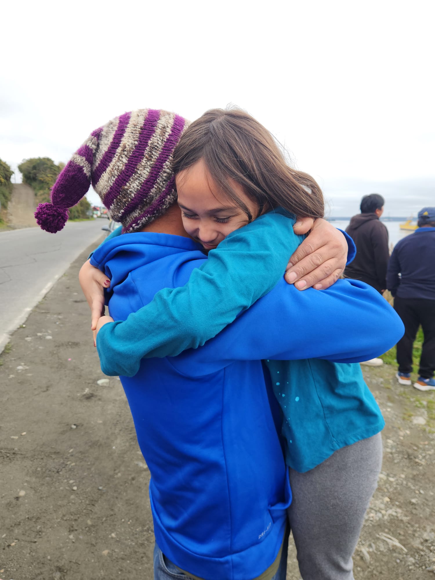 A man in a beanie hat hugs a little girl, lifting her from the ground.
