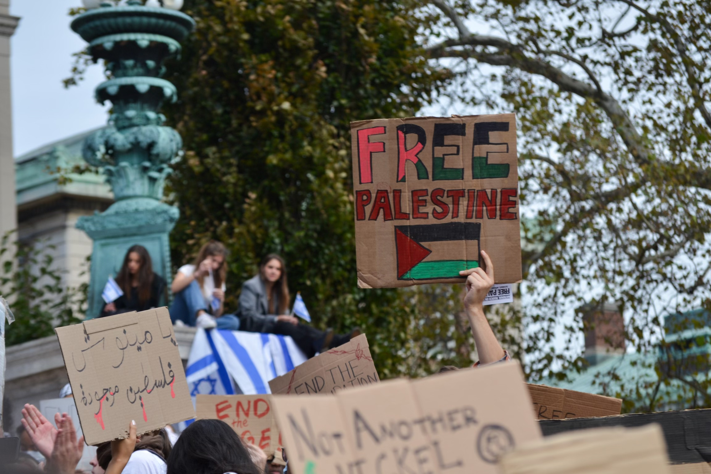 Students hold up carboard signs, with handwritten slogans like "Free Palestine."