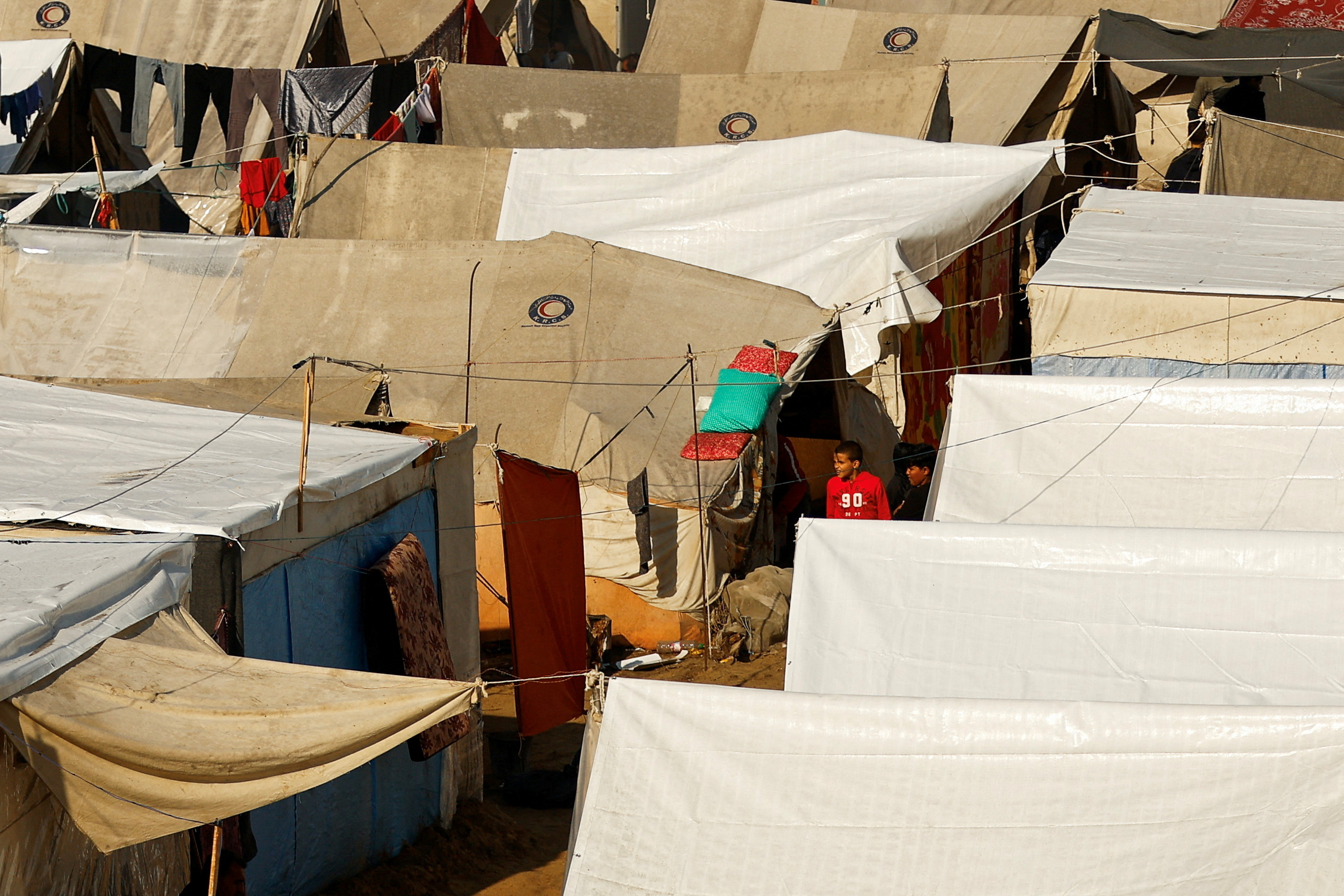 Children walk at a tent camp sheltering displaced Palestinians, amid the ongoing conflict between Israel and Palestinian Islamist group Hamas, following rainfall, in Khan Younis in the southern Gaza Strip