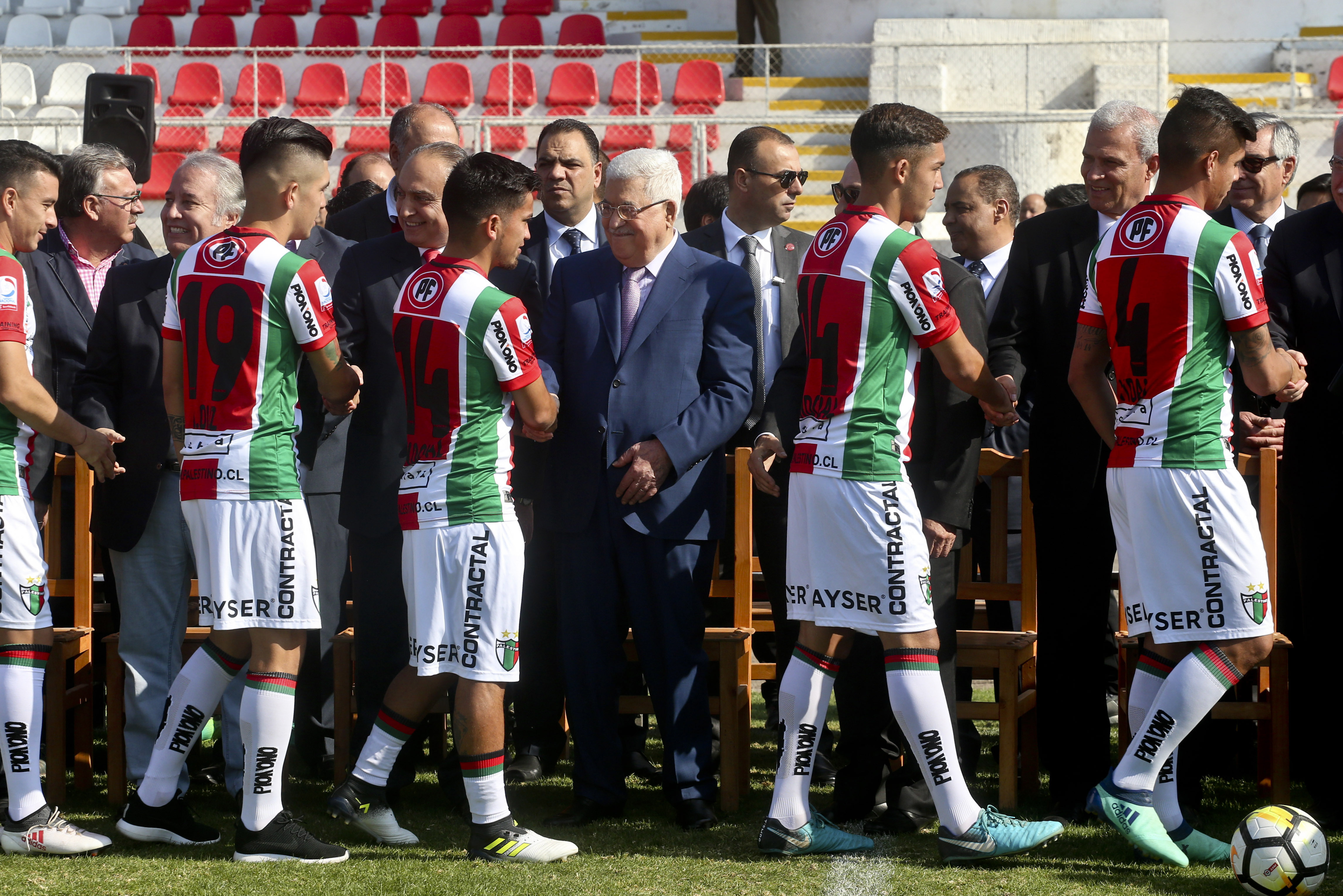 A row of soccer players walk along a line of politicians, shaking hands