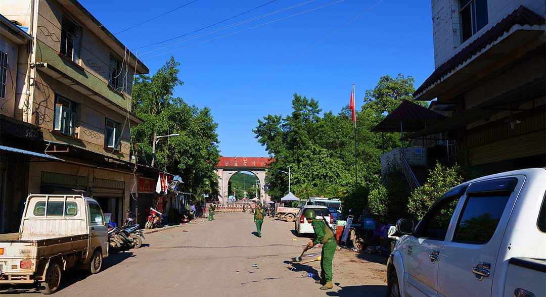 Members of MNDAA pictured in Chin Shwe Haw on the border of Myanmar and China. There are cars on the road and a gateway with Chinese lettering in the background