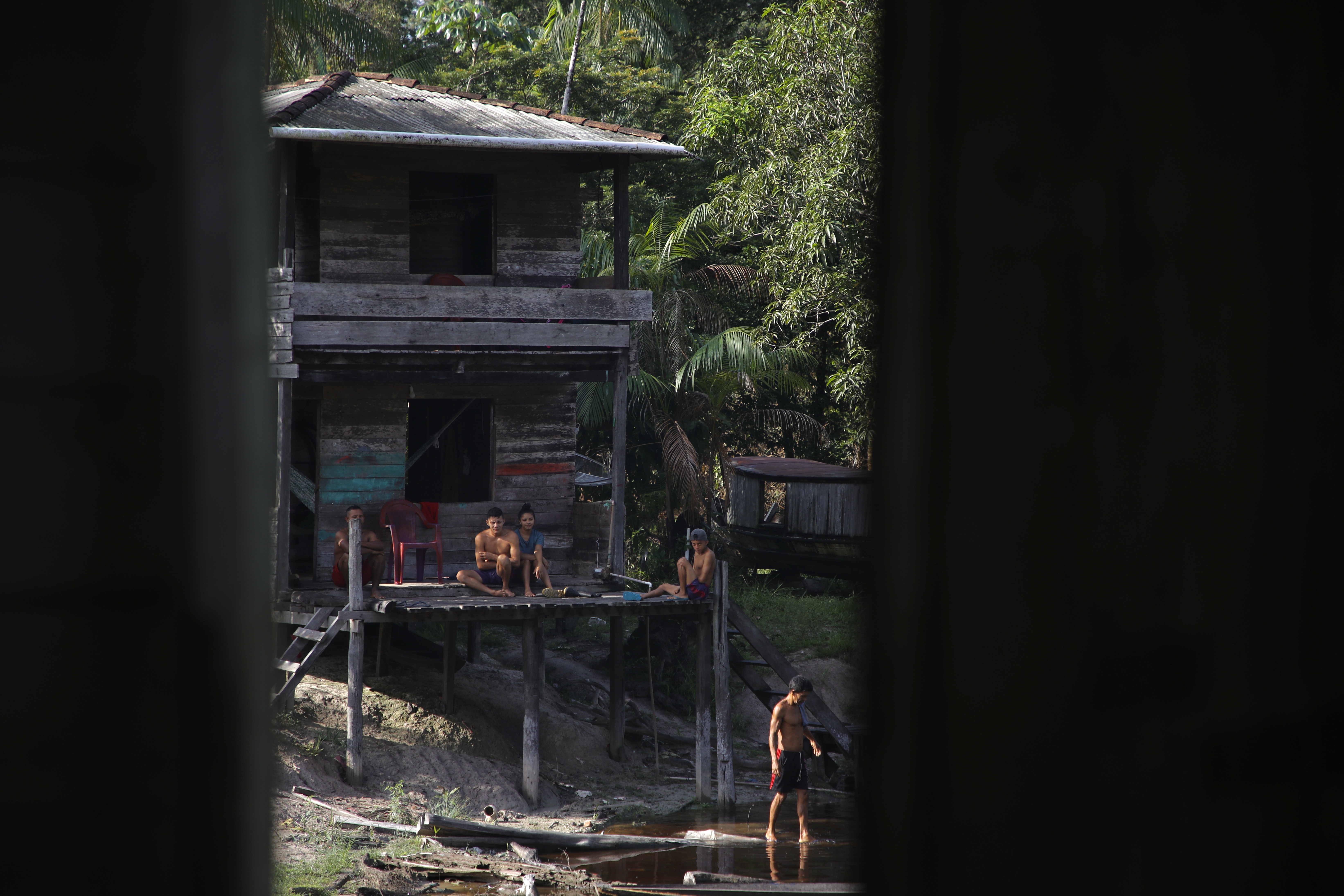 A wooden house on the water's edge is seen between two slats of wood.
