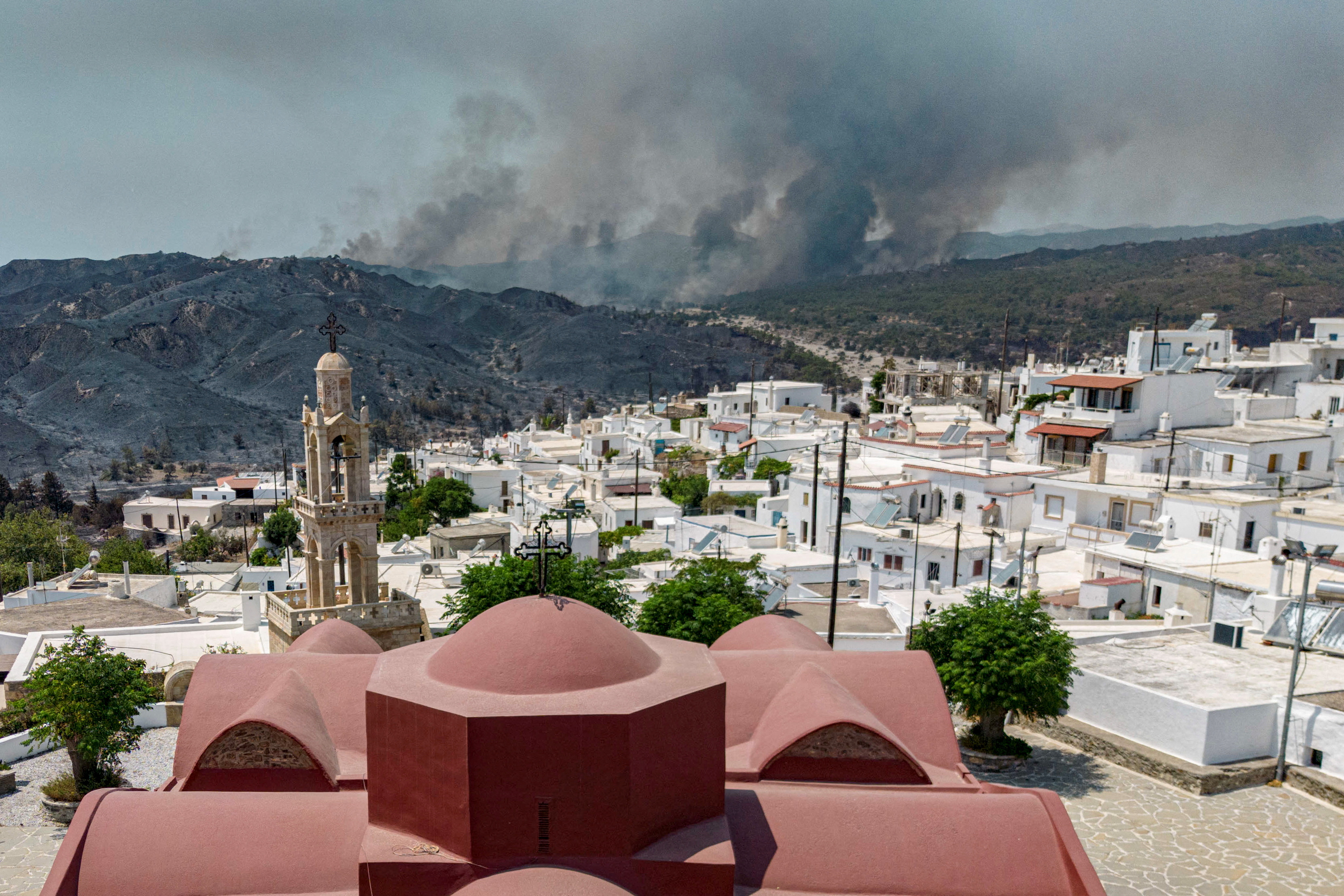 A view of the village of Asklipieio, as a wildfire burns in the background on the island of Rhodes, Greece, July 26