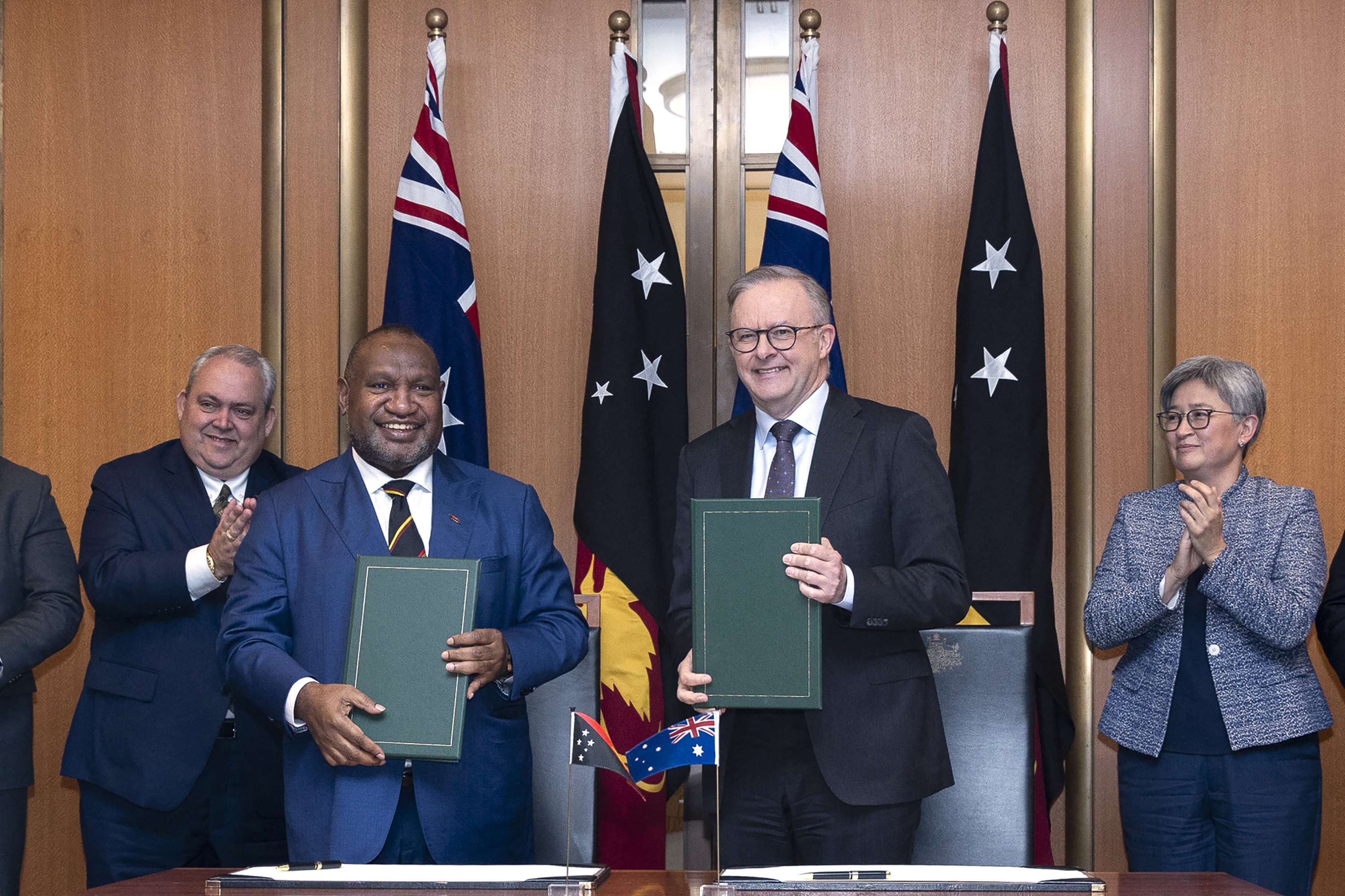 Australia's Prime Minister Anthony Albanese and PNG's Prime Minister James Marape at the official signing ceremony for the security pact. They are each holding a copy of the documents. Their countries flags are behind them.