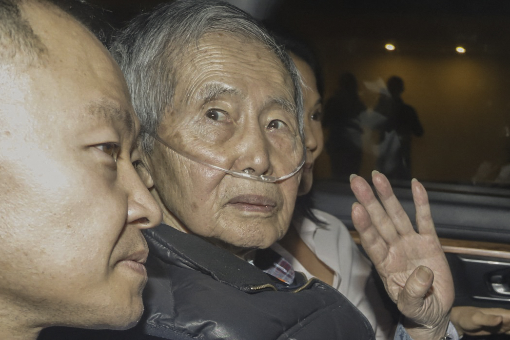 Alberto Fujimori waves from the car as he leaves prison. He is sitting between his son and daughter. His hair is white and his face looks gaunt.