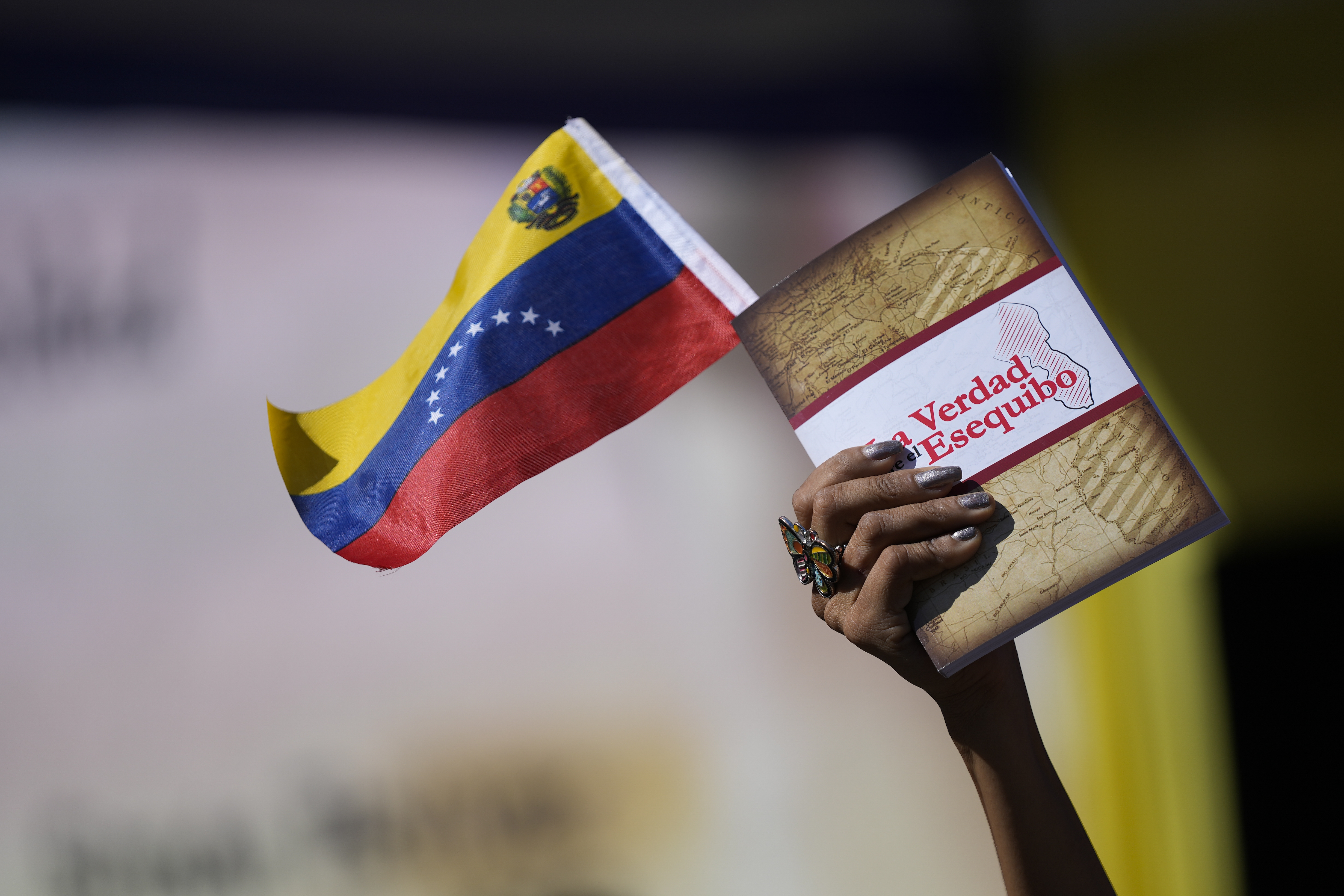 A woman holds a Venezuelan flag and a book about the Essequibo territory dispute in Caracas, Venezuela [File: Matias Delacroix/AP]