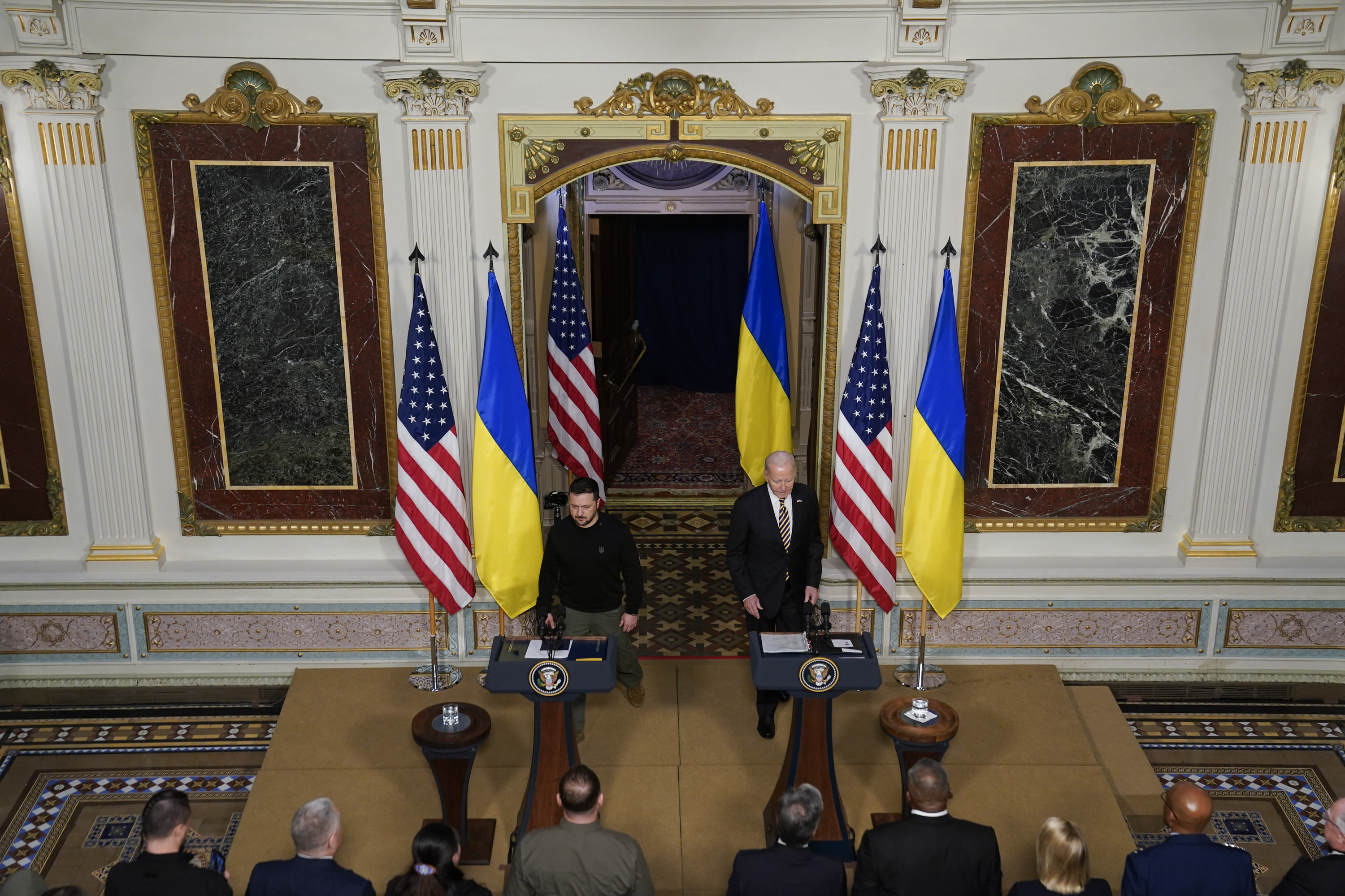 Volodymyr Zelenskyy and Joe Biden stand behind wooden podiums and in front of Ukrainian and US flags in a press conference at the White House.