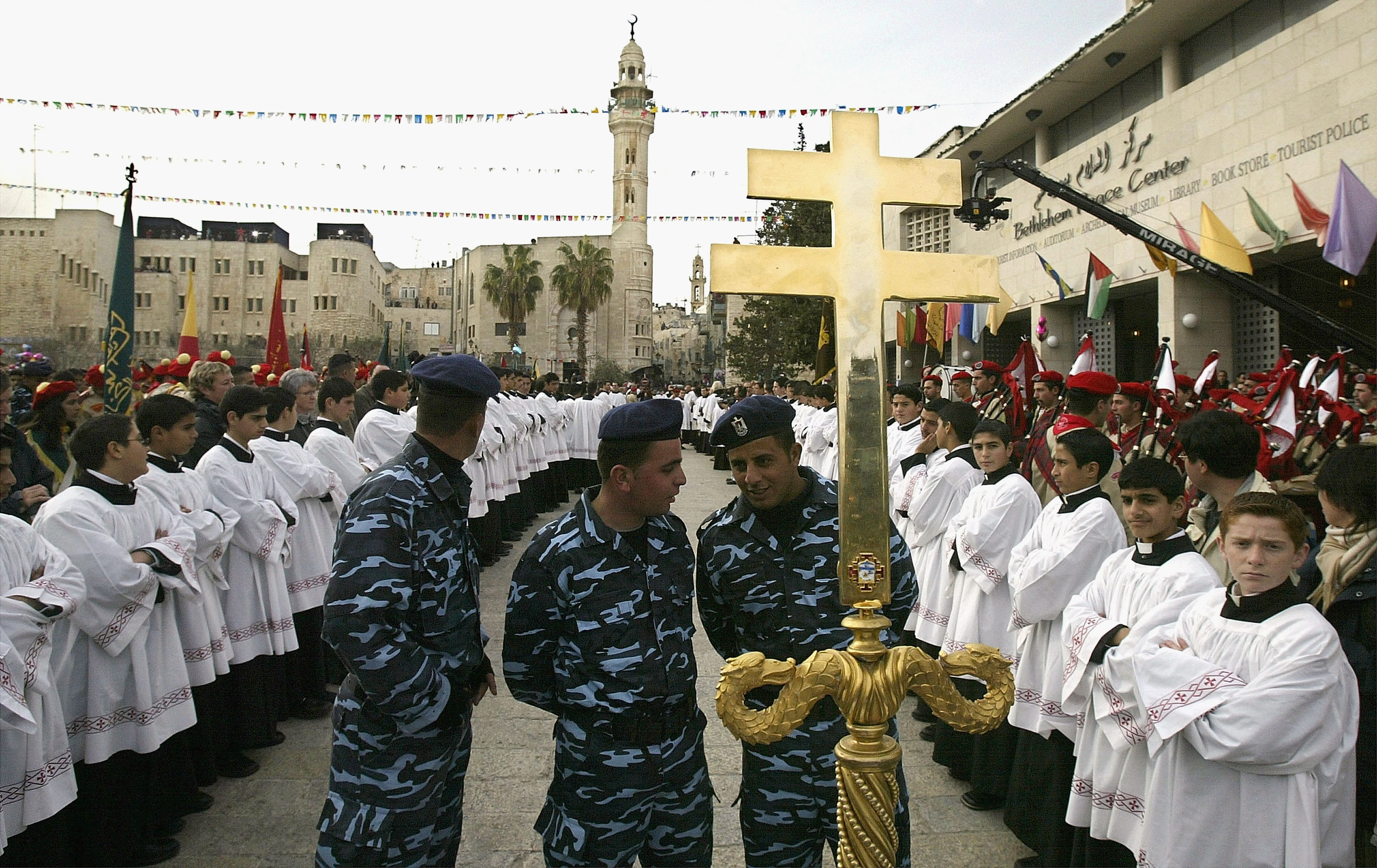 Palestinian Christian altar boys and Palestinian police wait the arrival of the Latin Patriarch, Michel Sabbah, during the annual Christmas Eve procession December 24, 2003 in Manger Square in the West Bank town of Bethlehem. The biblical town, believed to be the birthplace of Jesus, faces yet another gloomy Christmas in the face of more than three years of Palestinian-Israeli violent conflict. 
