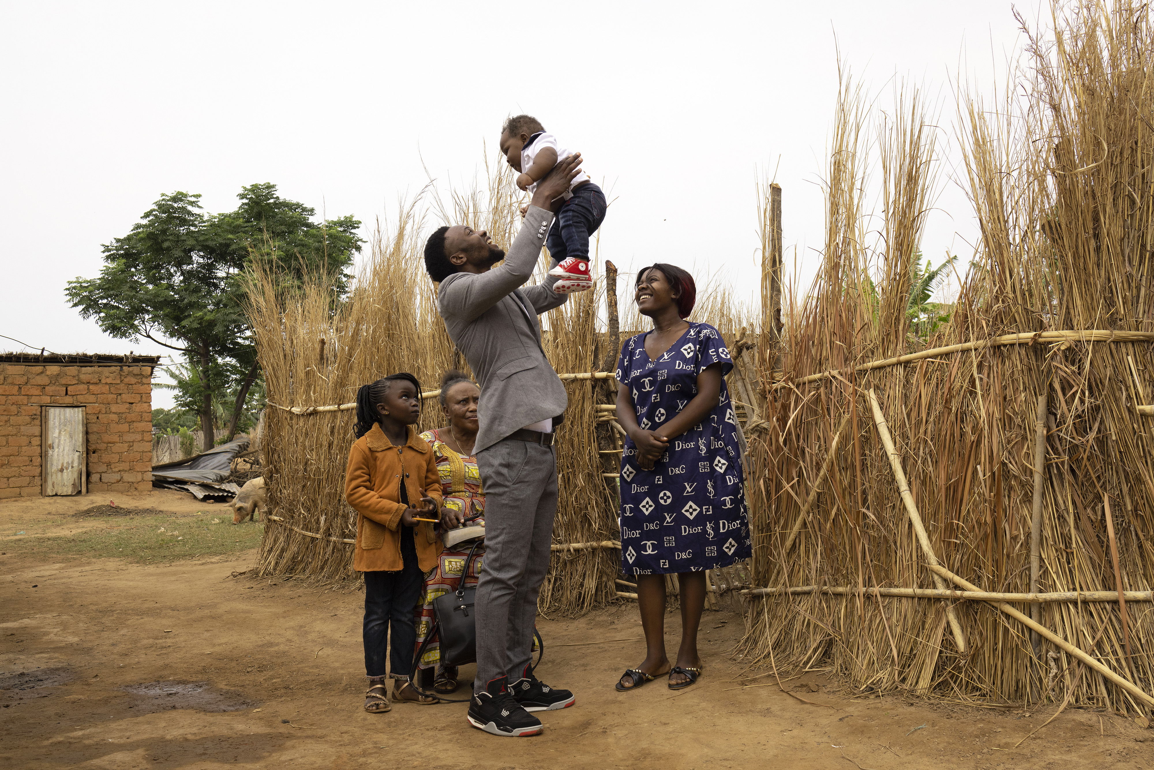 A young man holds a baby, standing next to women and a girl near a field in Zambia