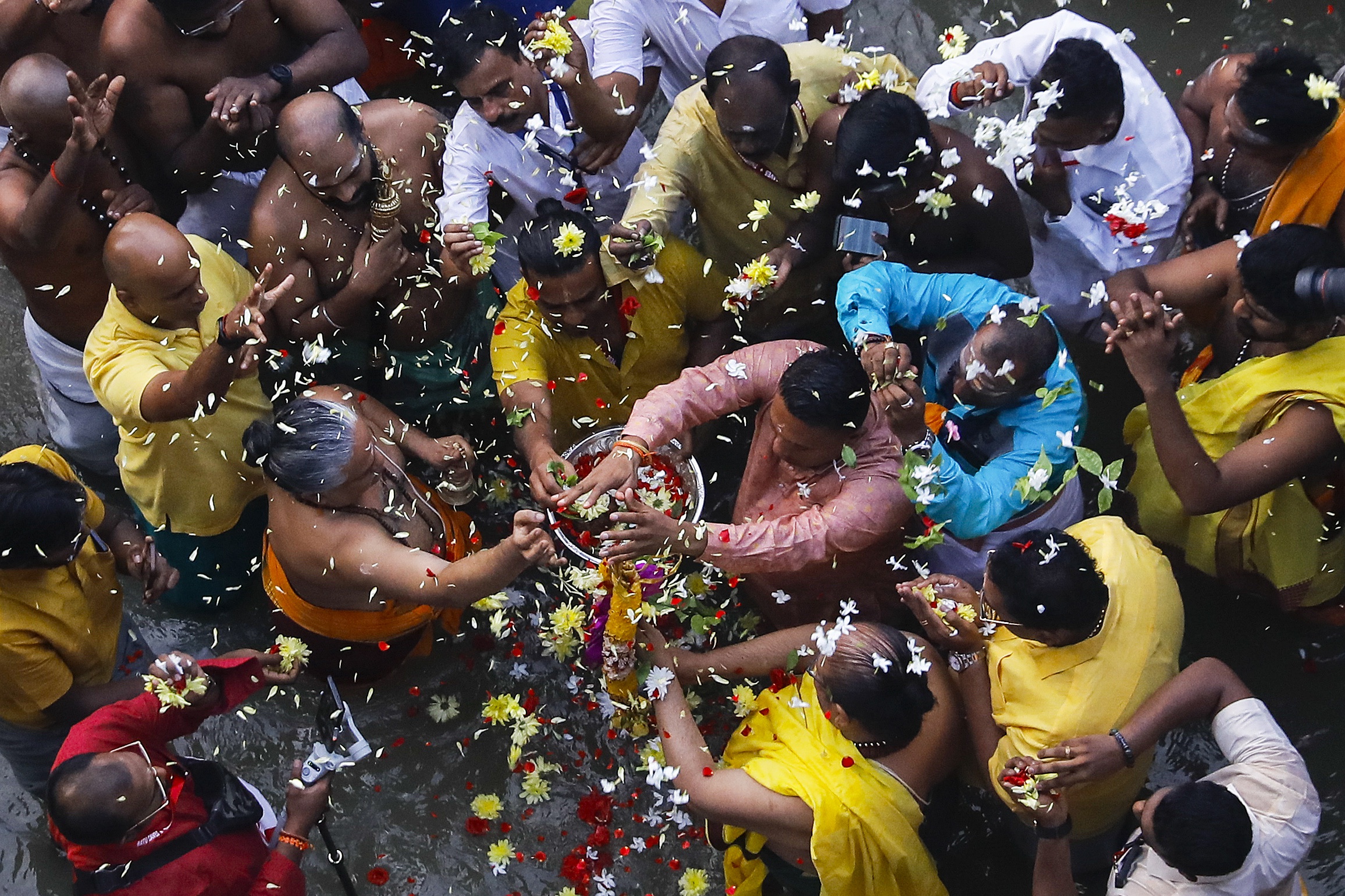 People praying in the river near the Batu Caves temple. They are pictured from above throwing flowers and petals.