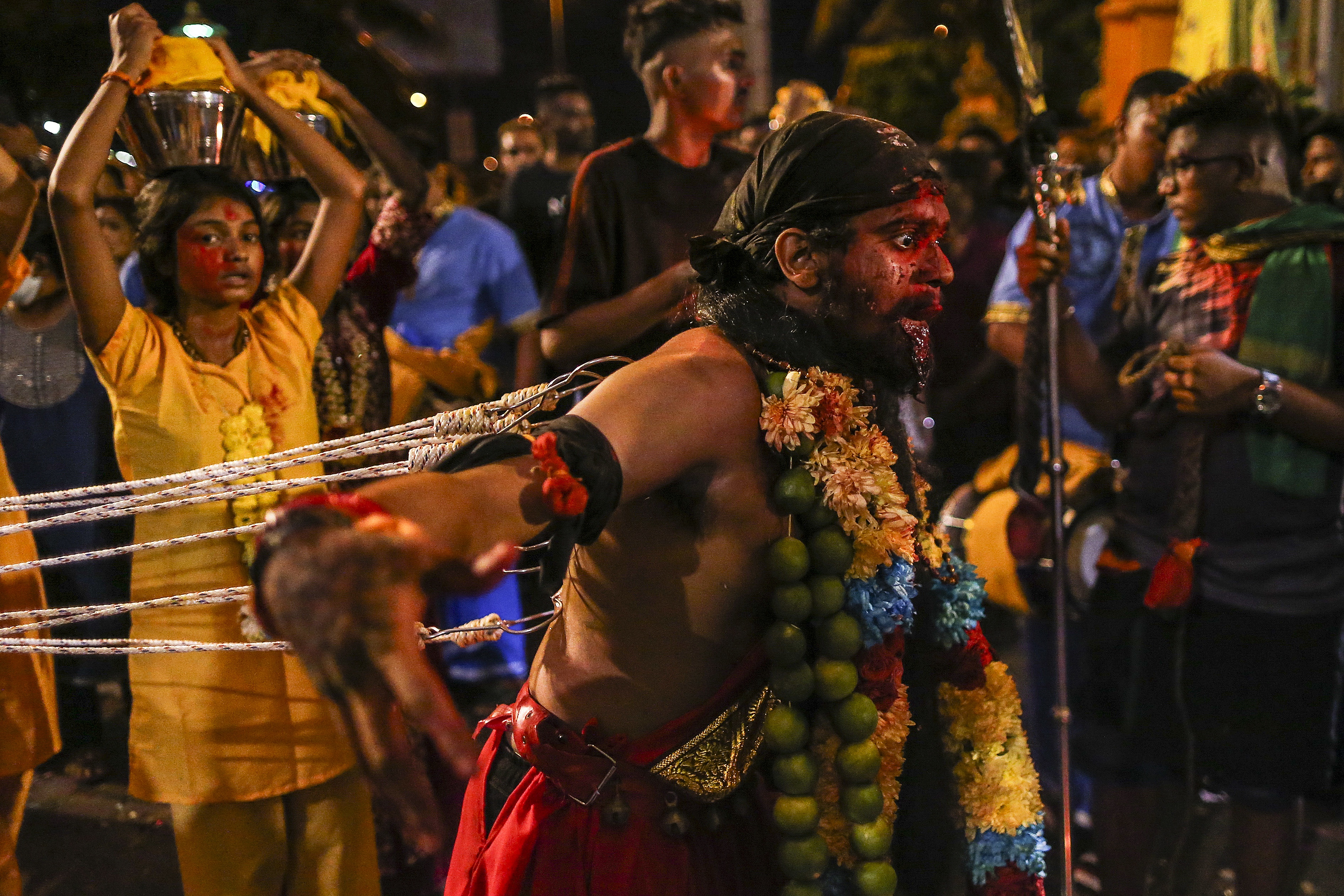 A man seen from the side with hooks attached to his back. People next to him are carrying milk on their heads