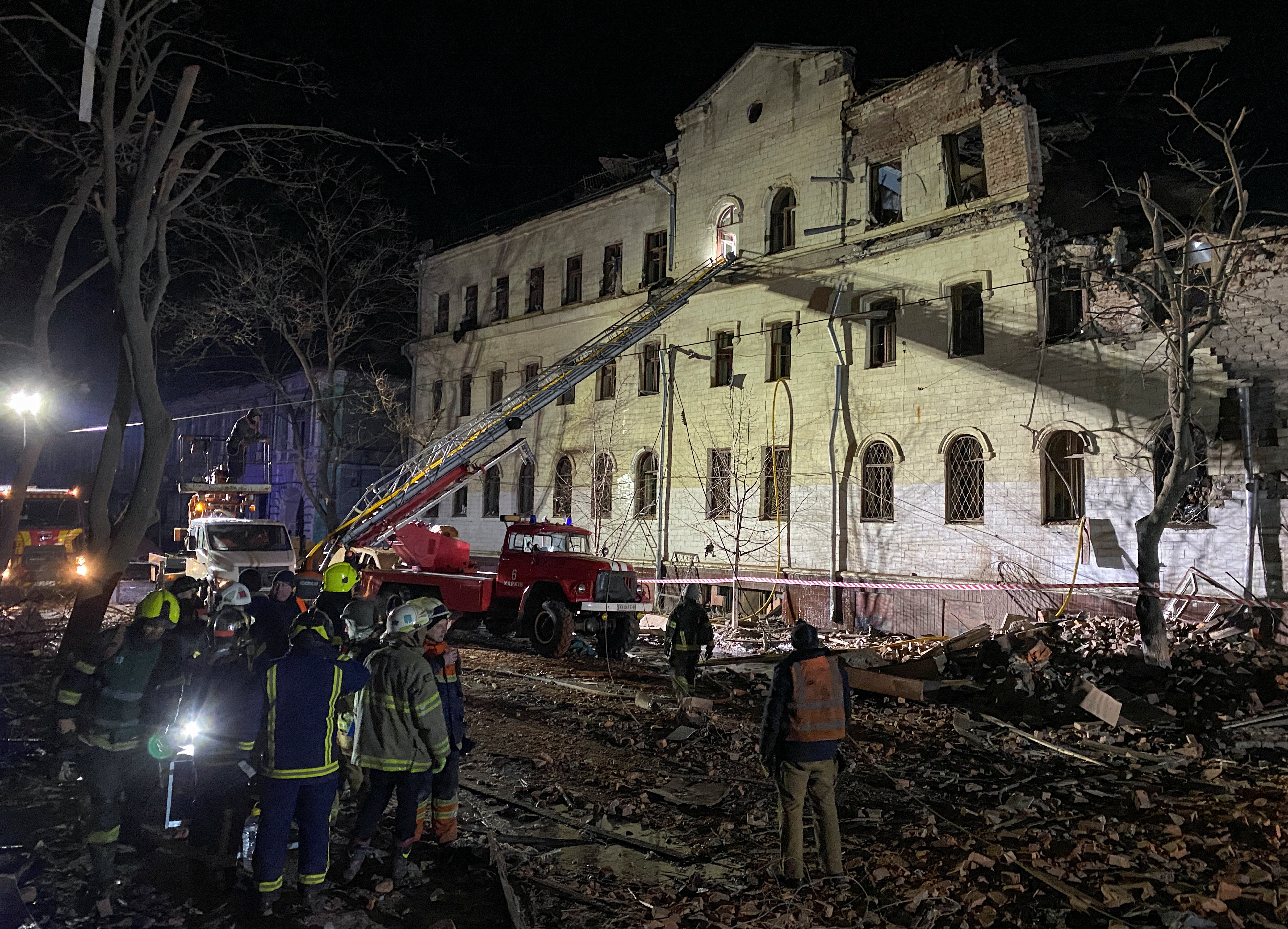 Rescuers working at a Kharkiv building hit by a Russian missile. It's dark but the building is lit up. There's an excavator.