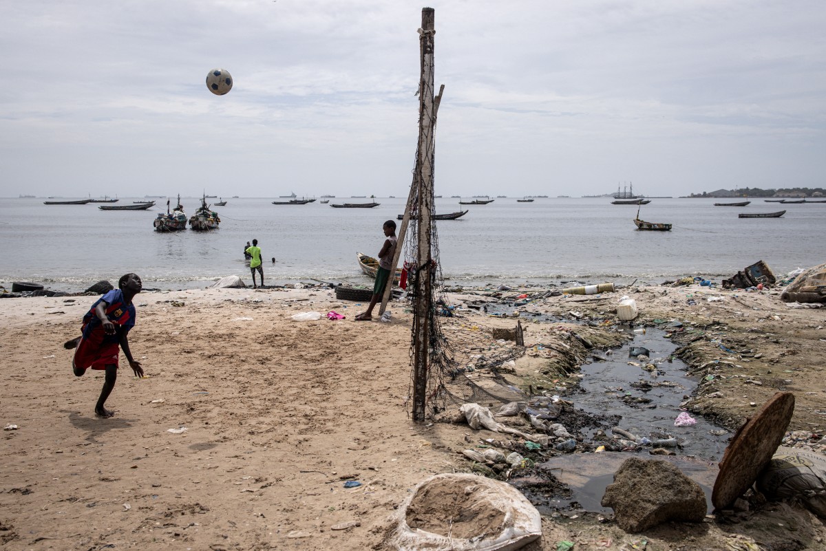 A young boy plays with a football next to a open sewage pipe along the polluted Hann Bay