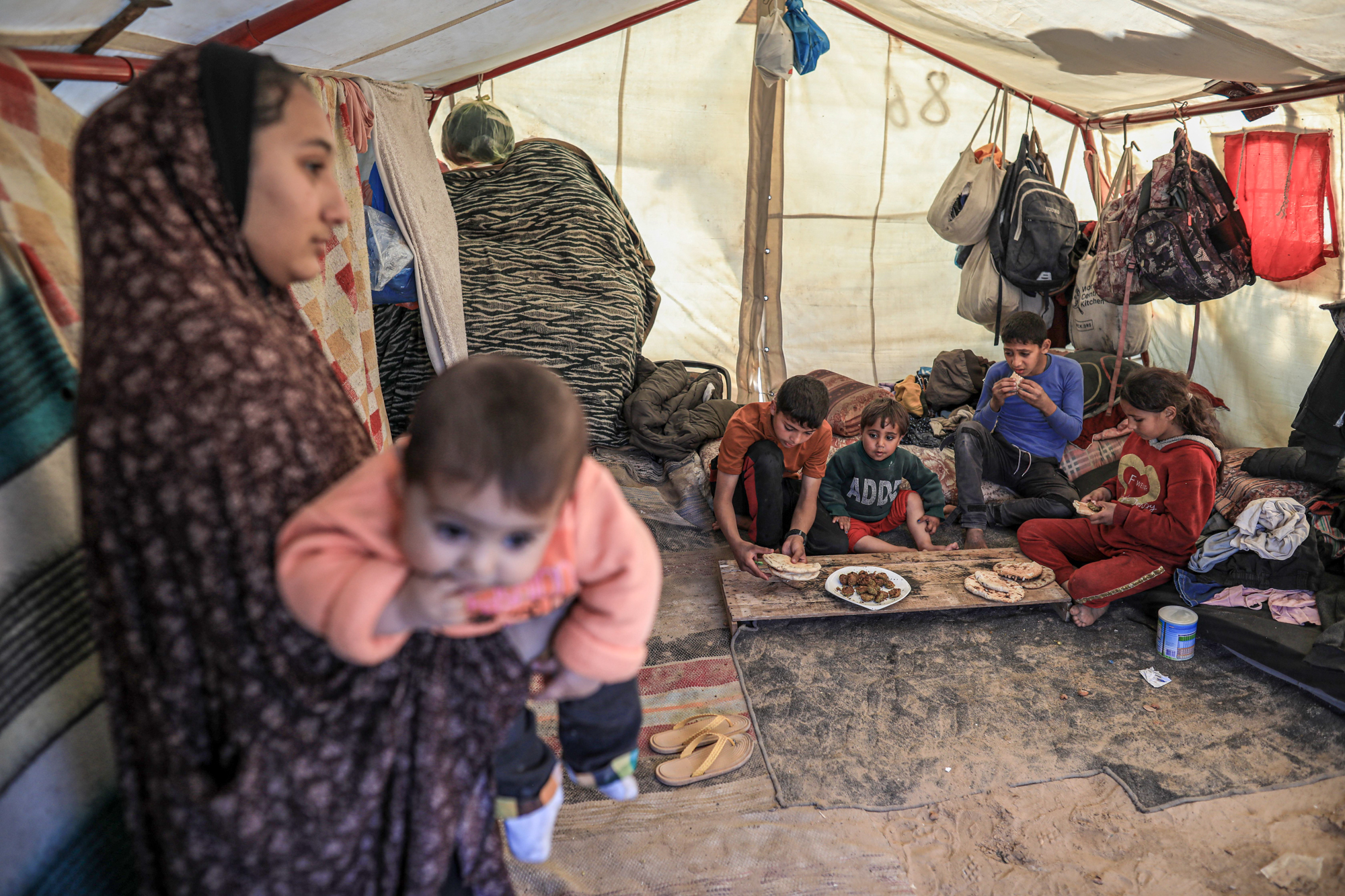 Nagham stands holding Toleen as her younger siblings eat