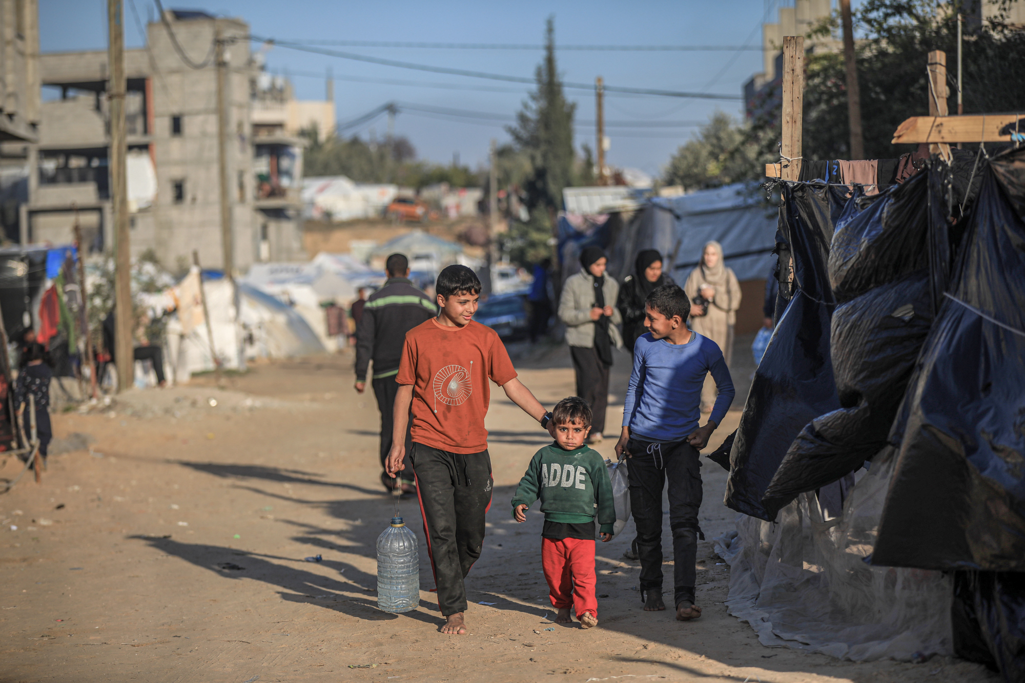 Mohammad carries a big bottle and walks along hiw two younger broters