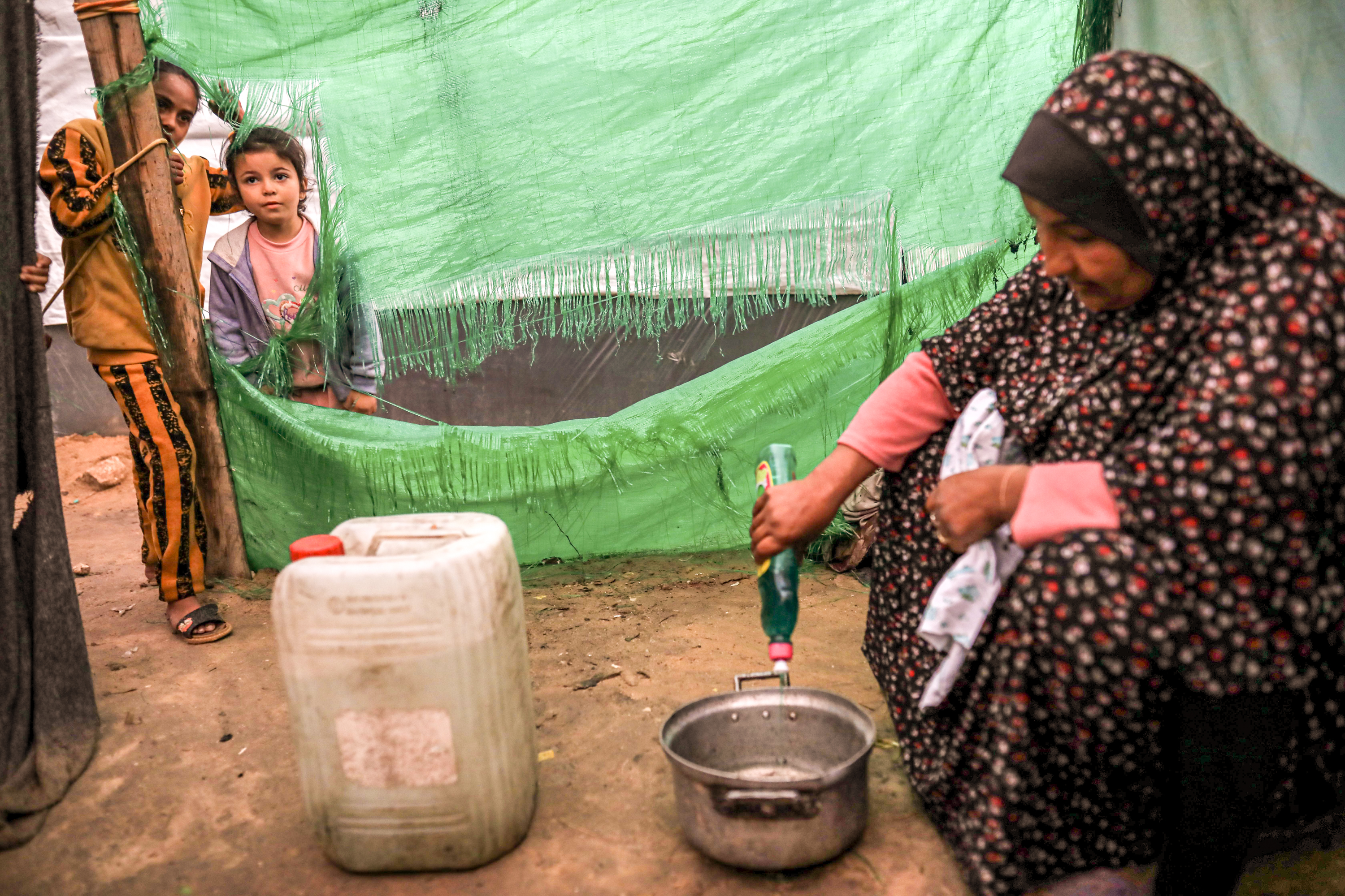 washing clothes in a little cooking pot with a tiny bit of dirty water