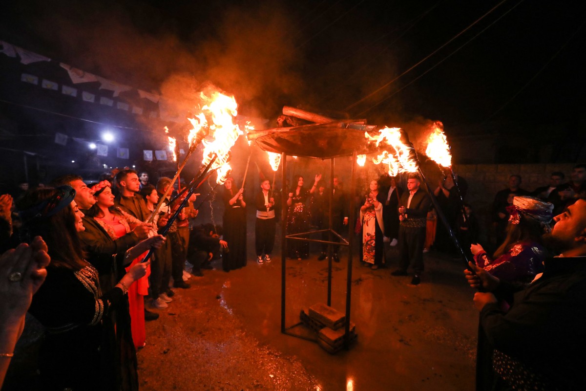 Syrian Kurds light up a pyre with torches during the celebration of Nowruz, the Persian New Year, in the Kurdish-majority city of Qamishli in Syria's northeastern Hasakeh province