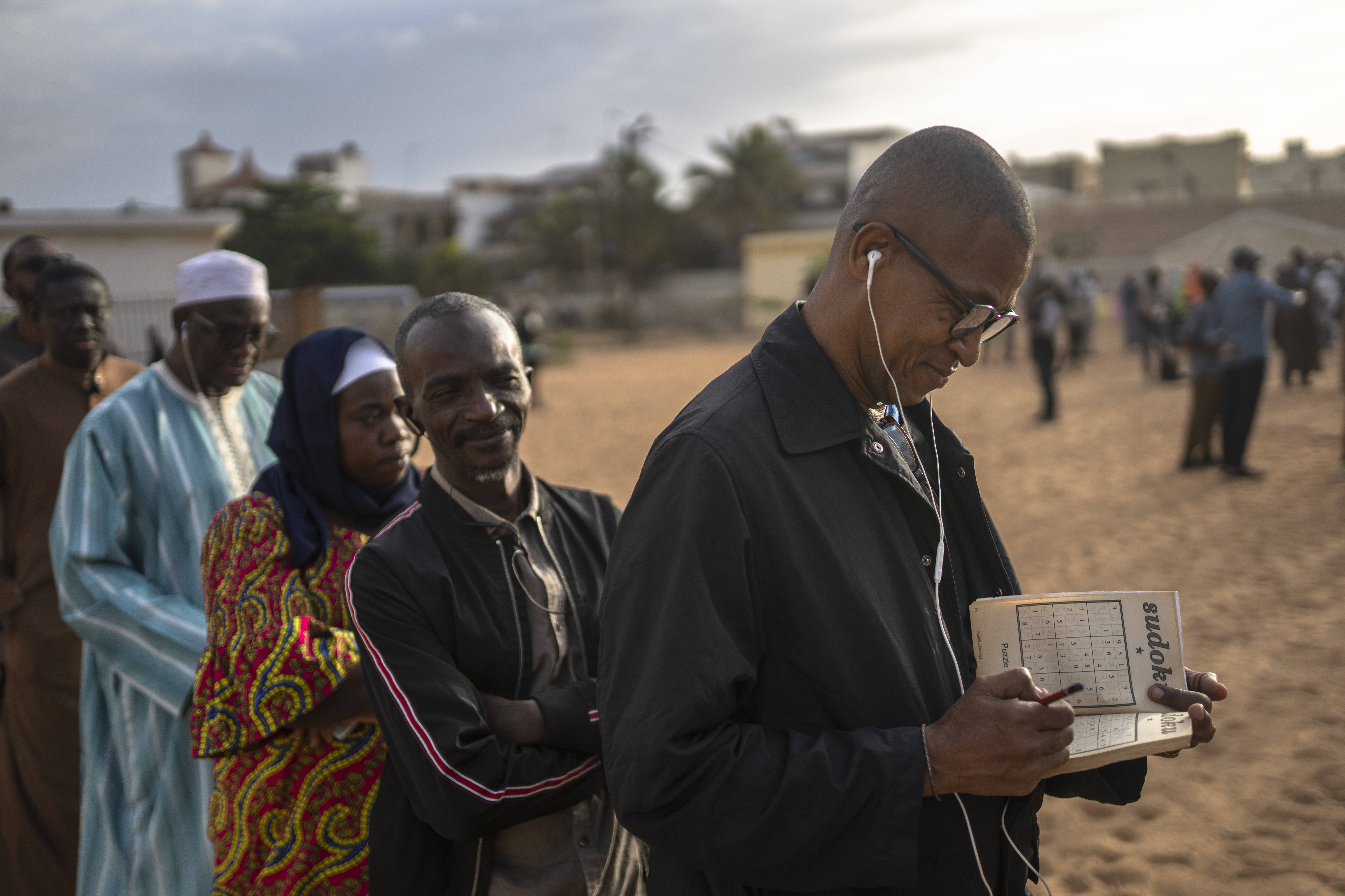 A man solves a sudoko riddle as he waits in line to cast his votes outside a polling station during the presidential elections, in Dakar, Senegal, Sunday, March 24, 2024. (AP Photo/Mosa'ab Elshamy)