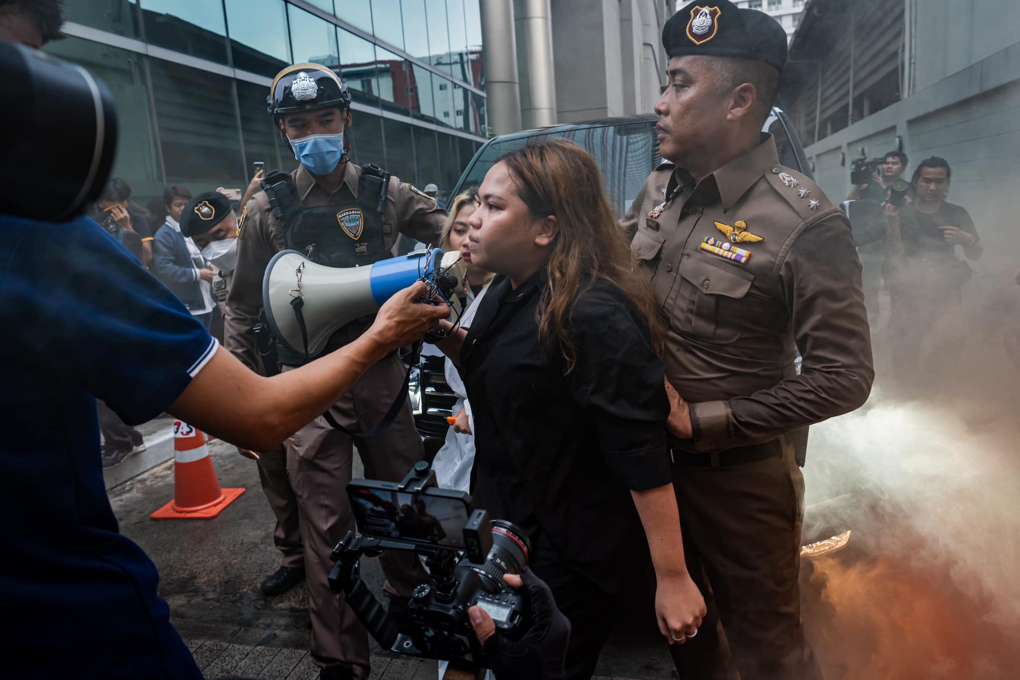 Netiporn surrounded by police. They are taking her away. The incident is being filmed by the media. 