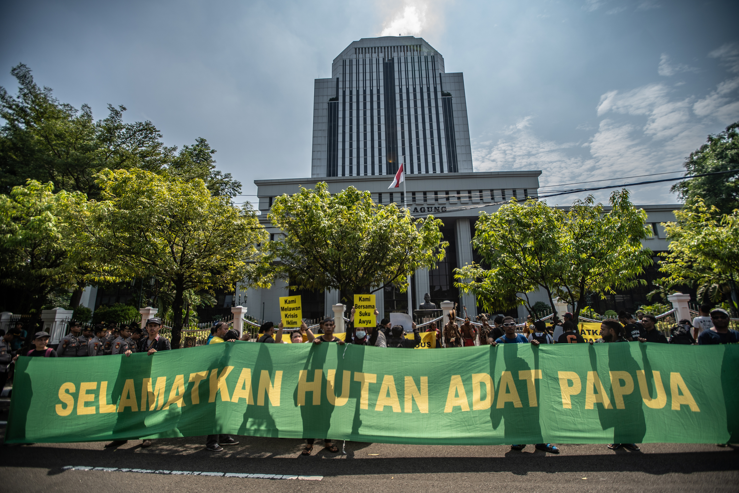 Activists standing with a giant green banner reading Selamatkan Hutan Adat Papua [Save Papua's Customary Forest]