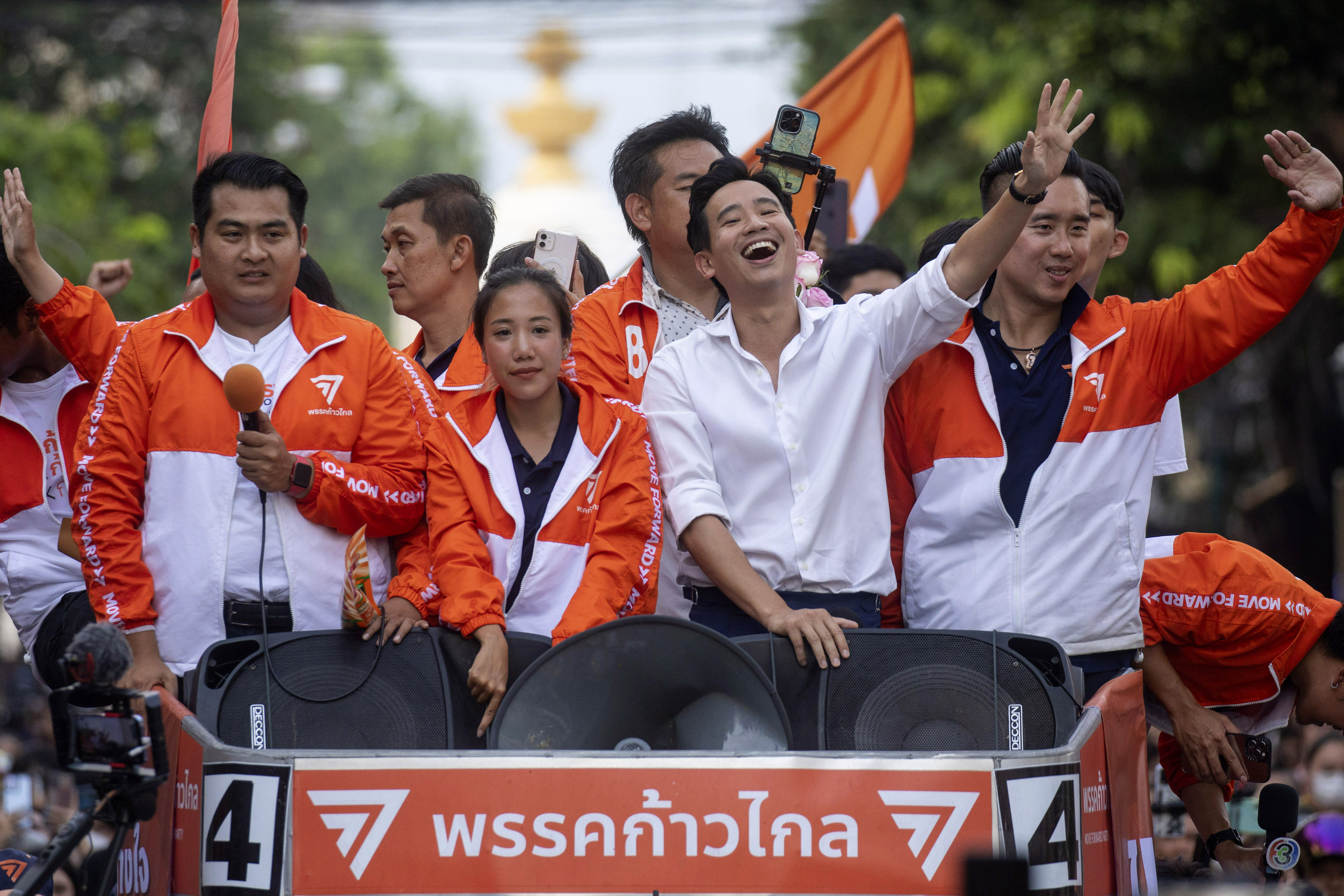 Move Forward celebrating its election victory on an open-top vehicle ride through Bangkok. Leader Pita Limjaroenrate is in front. They are waving and smiling at the crowds.