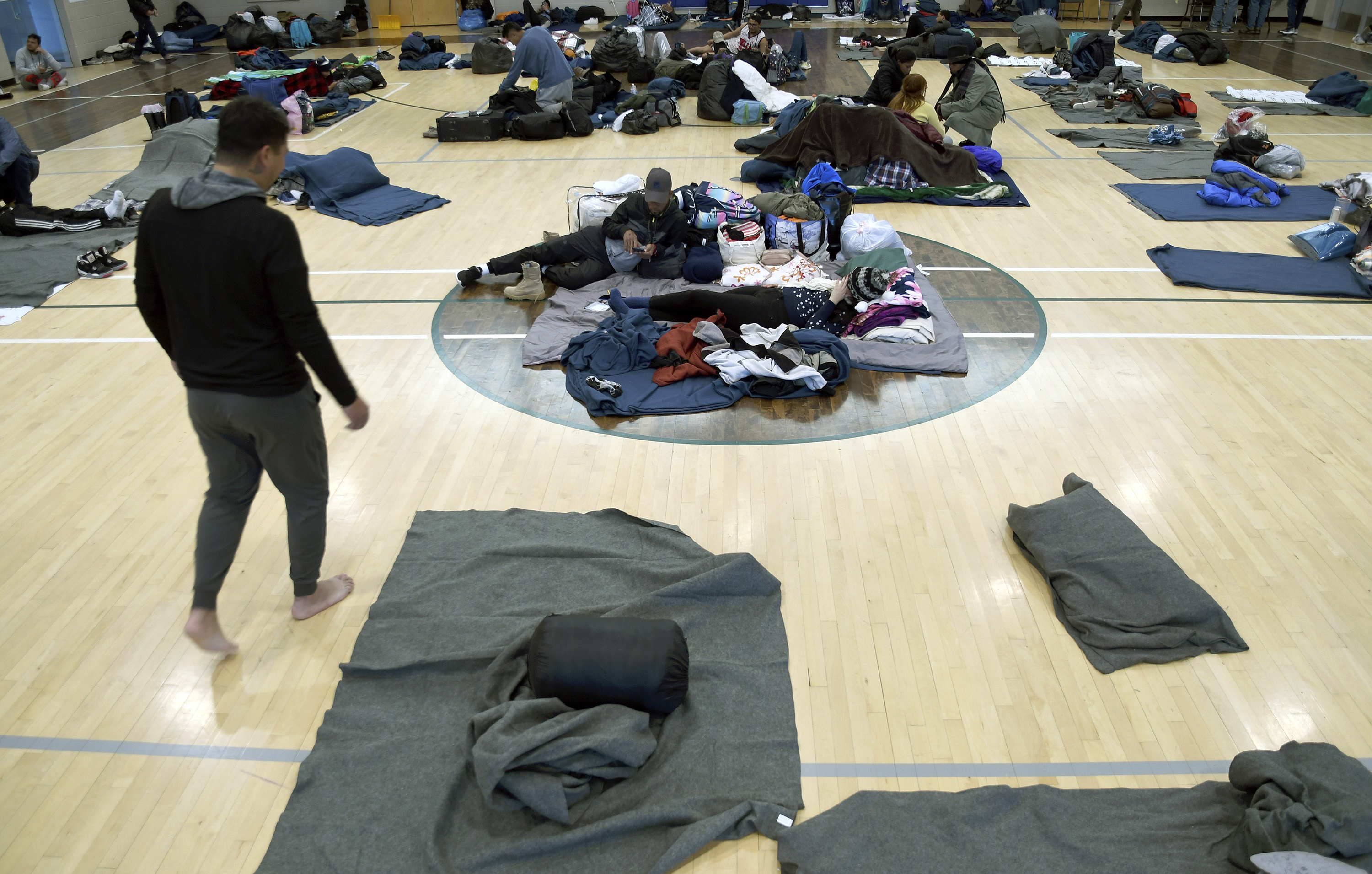Migrants and asylum seekers rest on mats on the glossy wooden floor of a gymnasium.