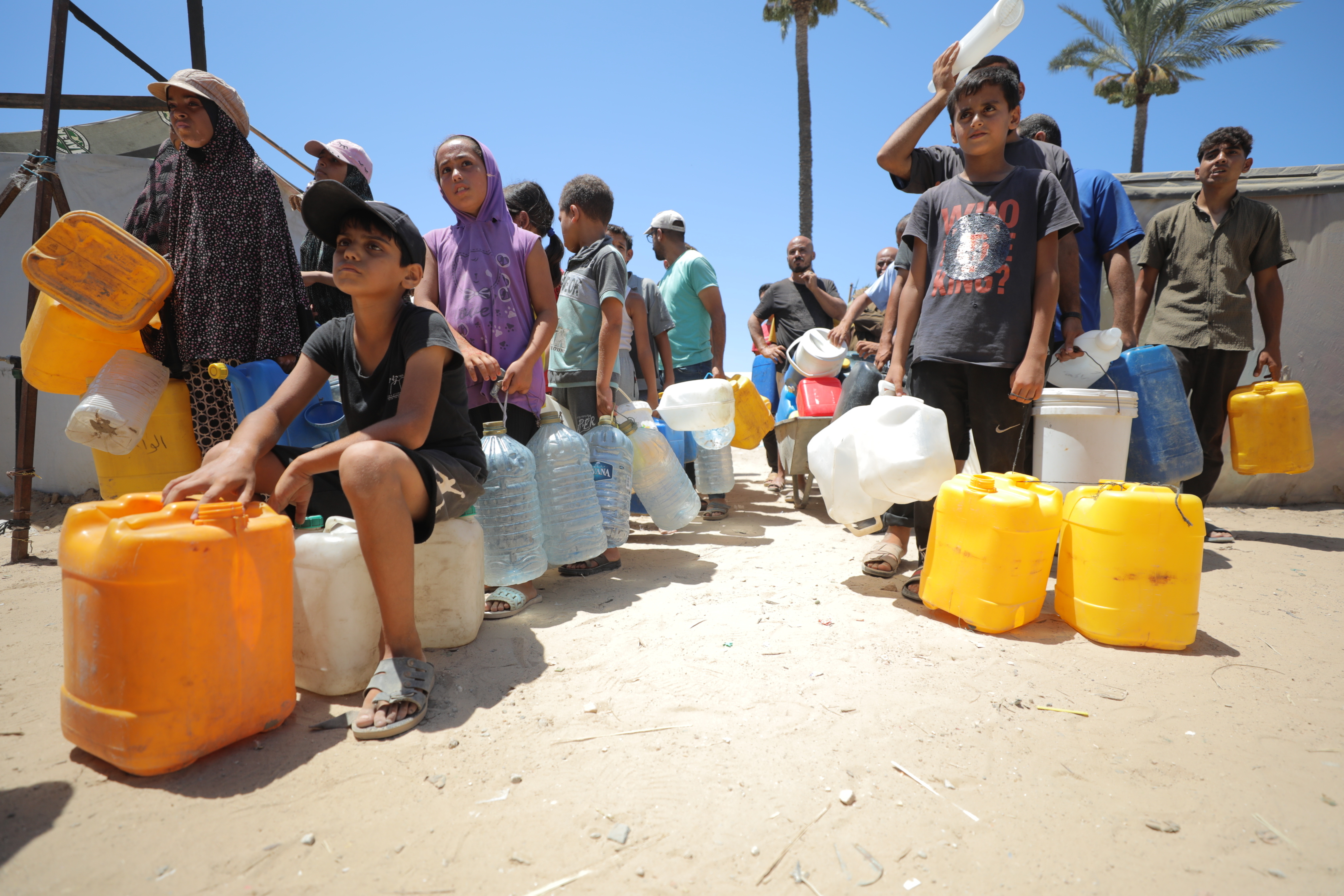 Palestinians who had to migrate to the city in the central part of Gaza to protect themselves from Israeli attacks on Gaza and to ensure their safety wait in queues to receive clean drinking water