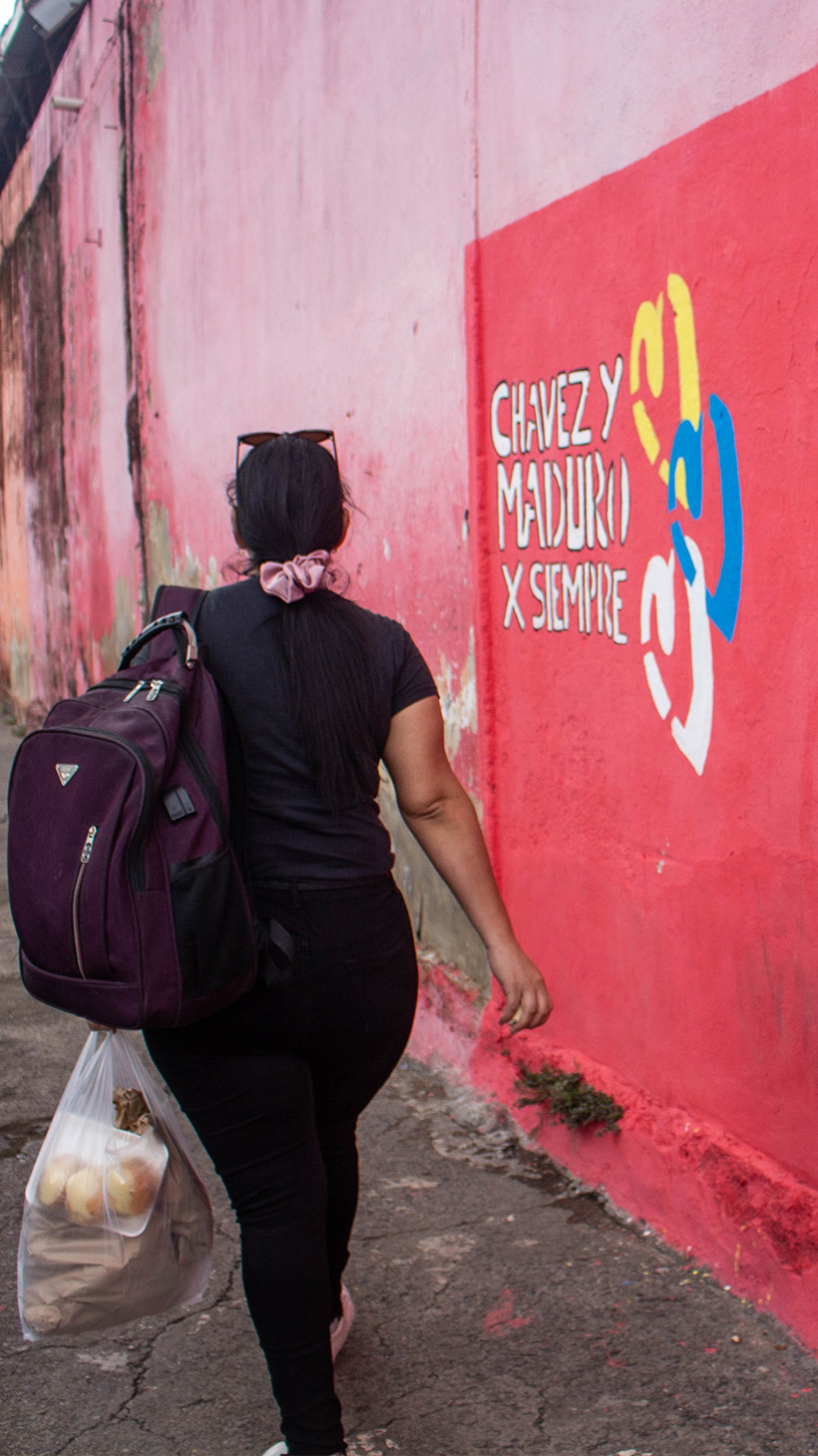 A woman walks past slogans painted on a wall next to a sidewalk, advertising Maduro's campaign.