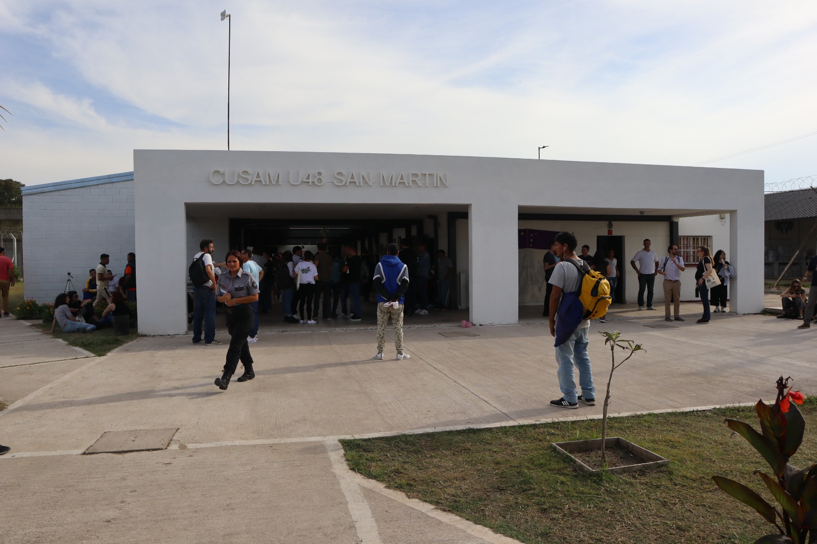 People stream in and out of a low-slung concrete building, labelled, "CUSAM U48 San Martin"