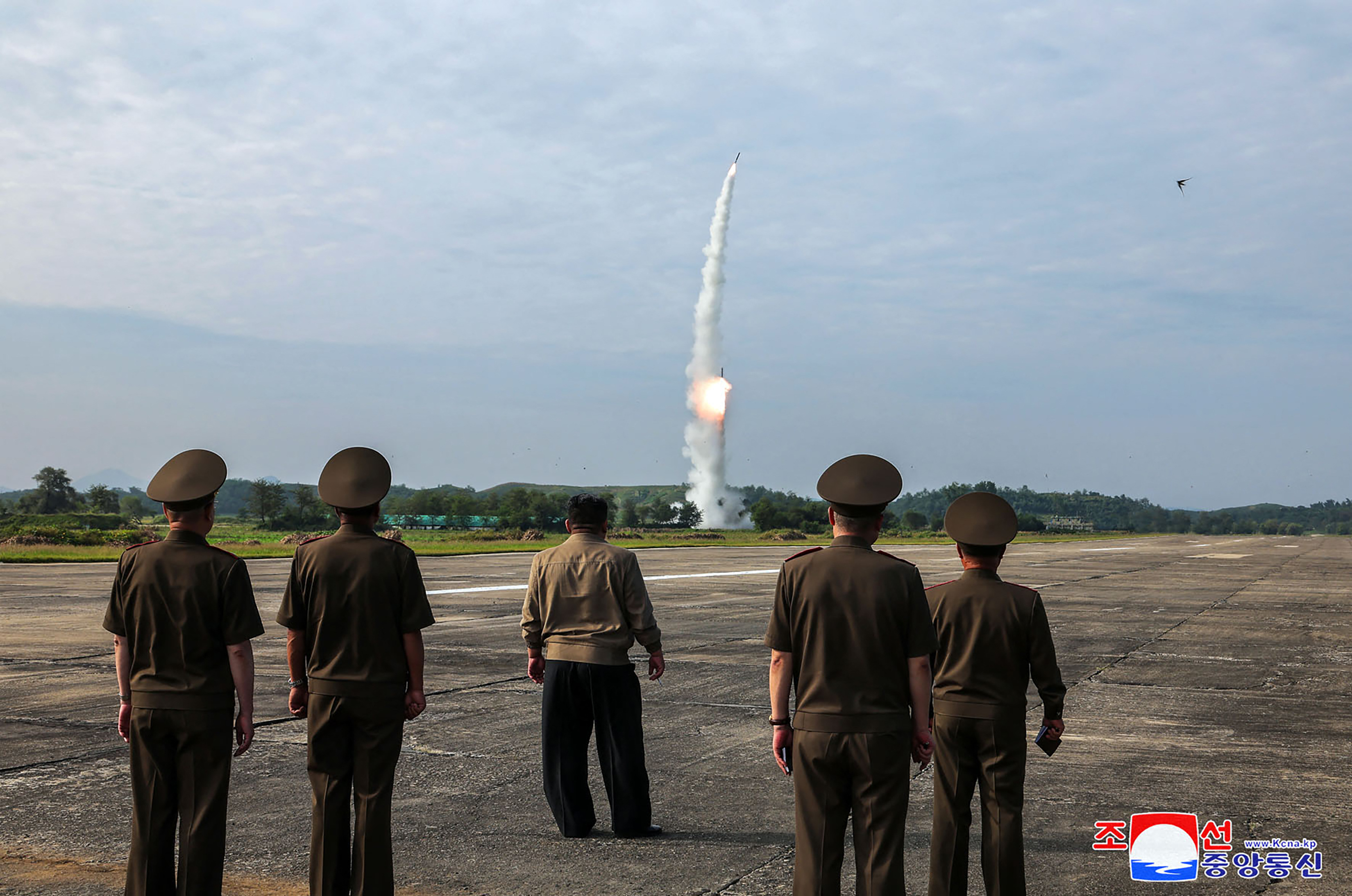 Kim Jong Un watching the missile test. It is taking off in the distance. Kim and a group of military officials are watching