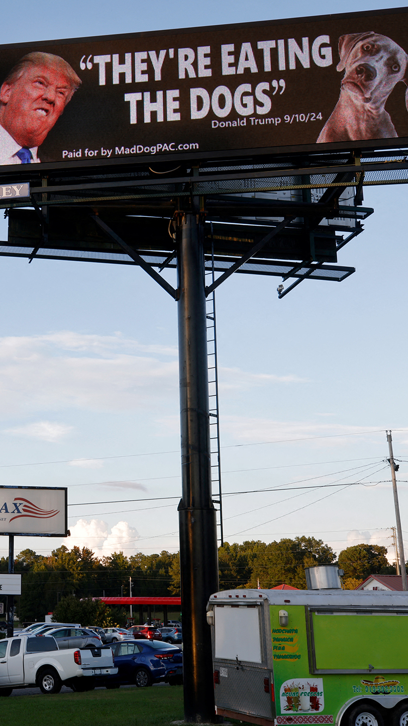 A billboard features Donald Trump's face next to a dog's, with the quote, "They're eating the dogs"