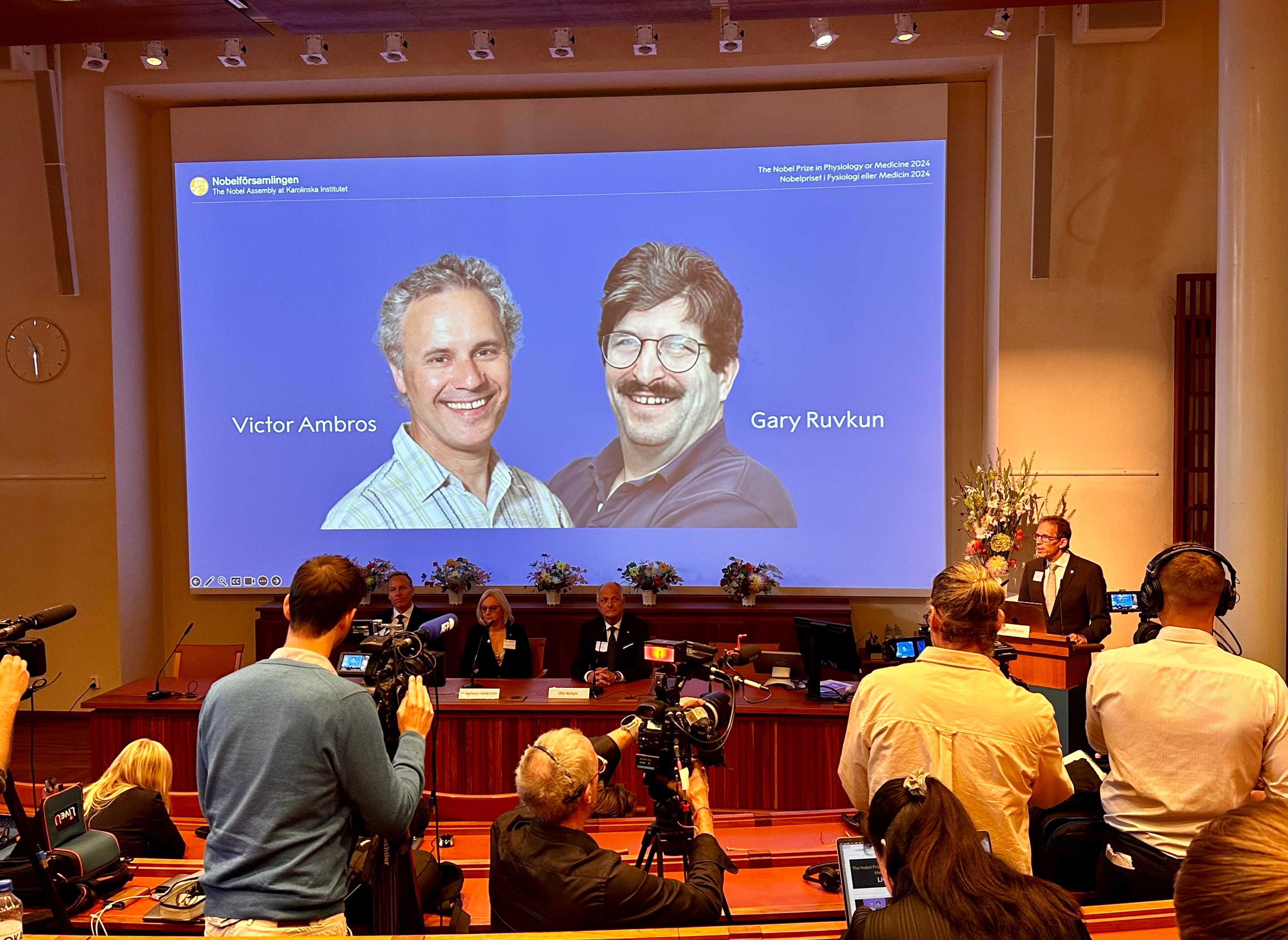 The secretary of the Nobel Assembly announces the winners of the 2024 Nobel Prize in Physiology or Medicine, Victor Ambros and Gary Ruvkun, whose photos are projected onto a screen