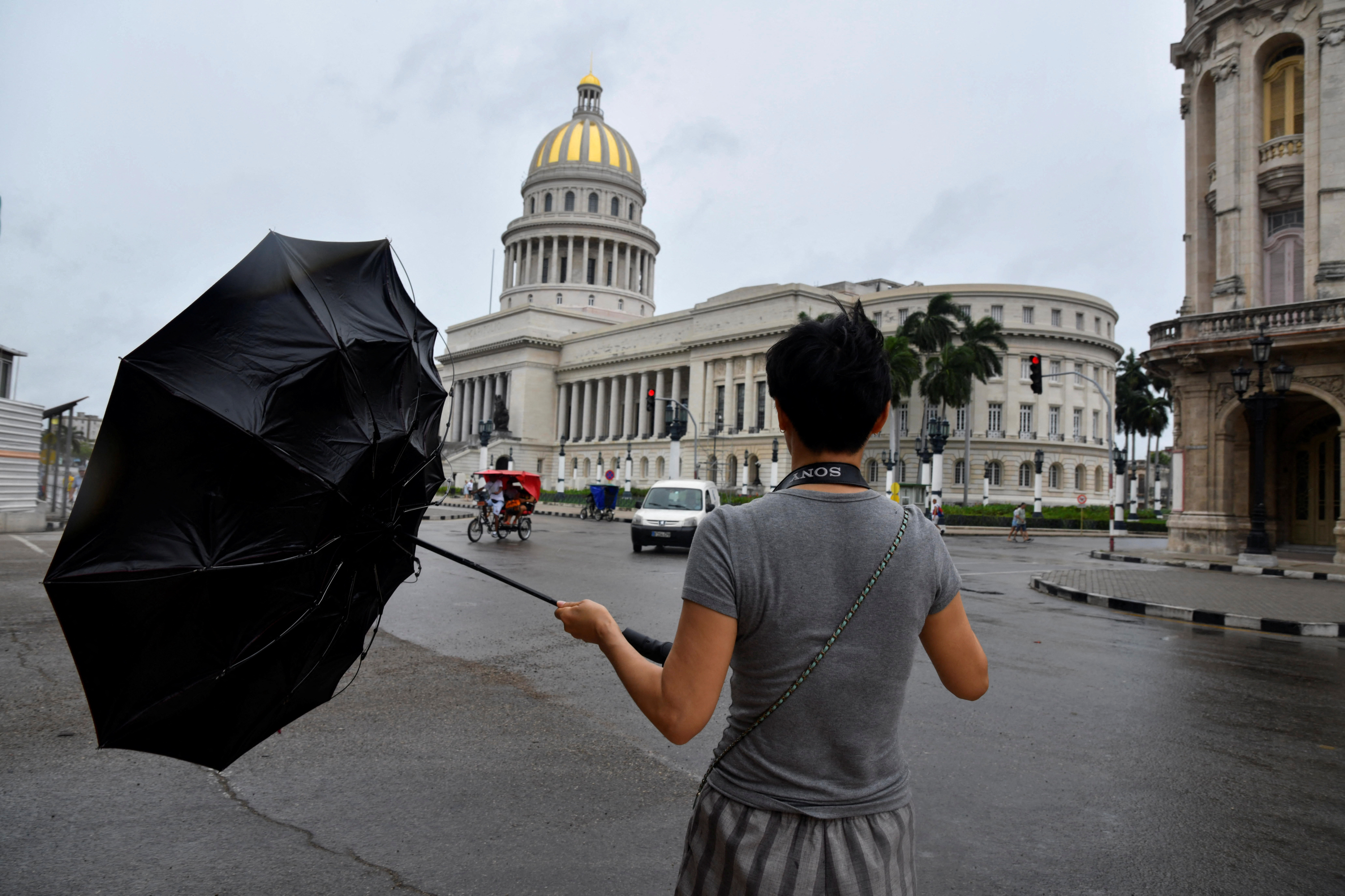 A pedestrian has their umbrella turned inside out by the wind.