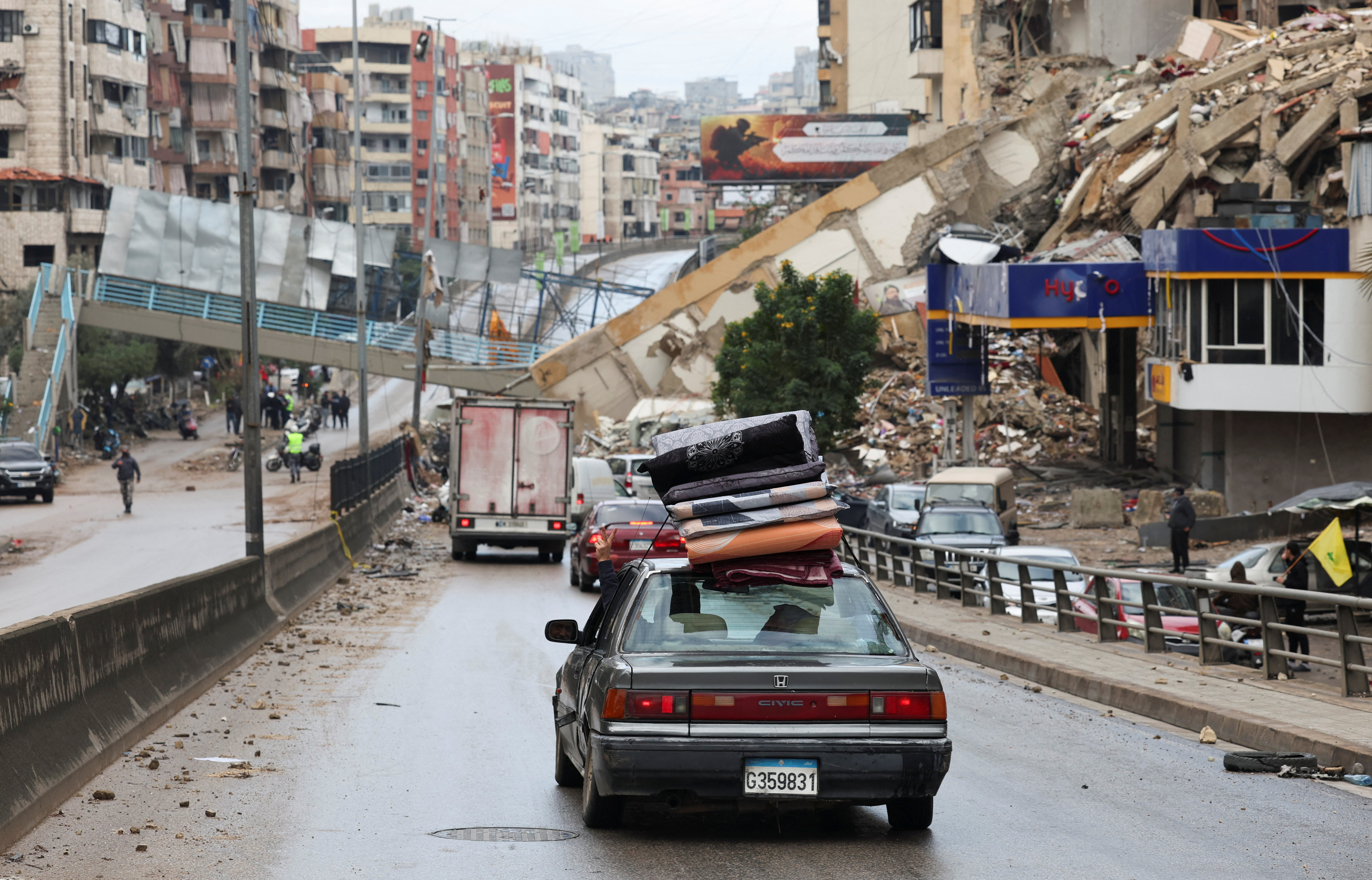 A vehicle transporting mattresses drives past a damaged pedestrian bridge