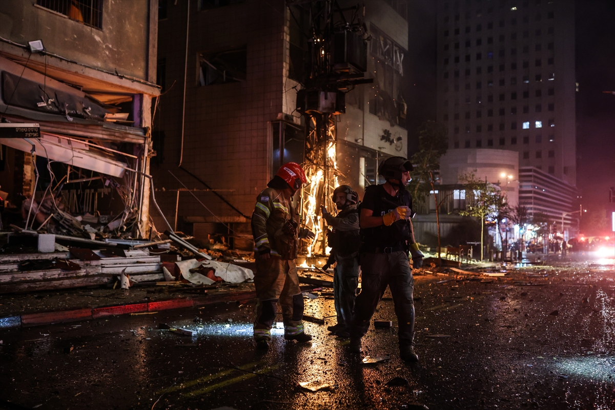 firefighters stand near a burning power pole at night