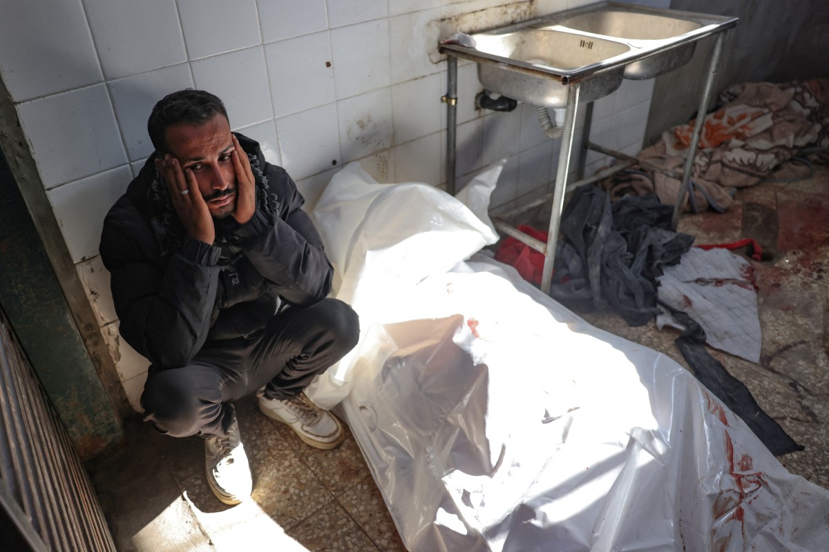 A Palestinian man sits next to the body of a person killed in an Israeli strike inside Al-Aqsa Martyrs Hospital in Deir el-Balah