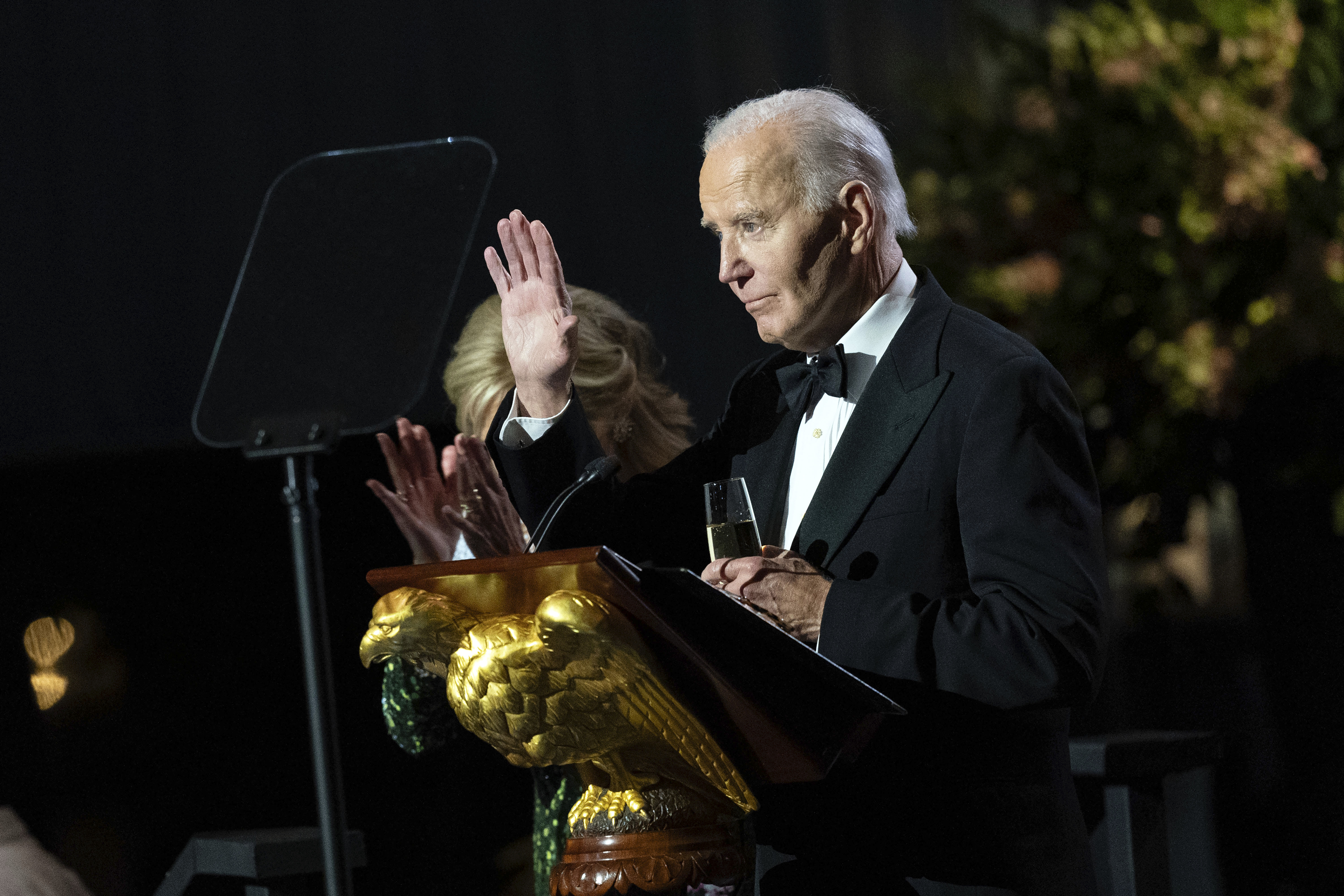 Joe Biden waves from behind a podium with a golden eagle at its base.
