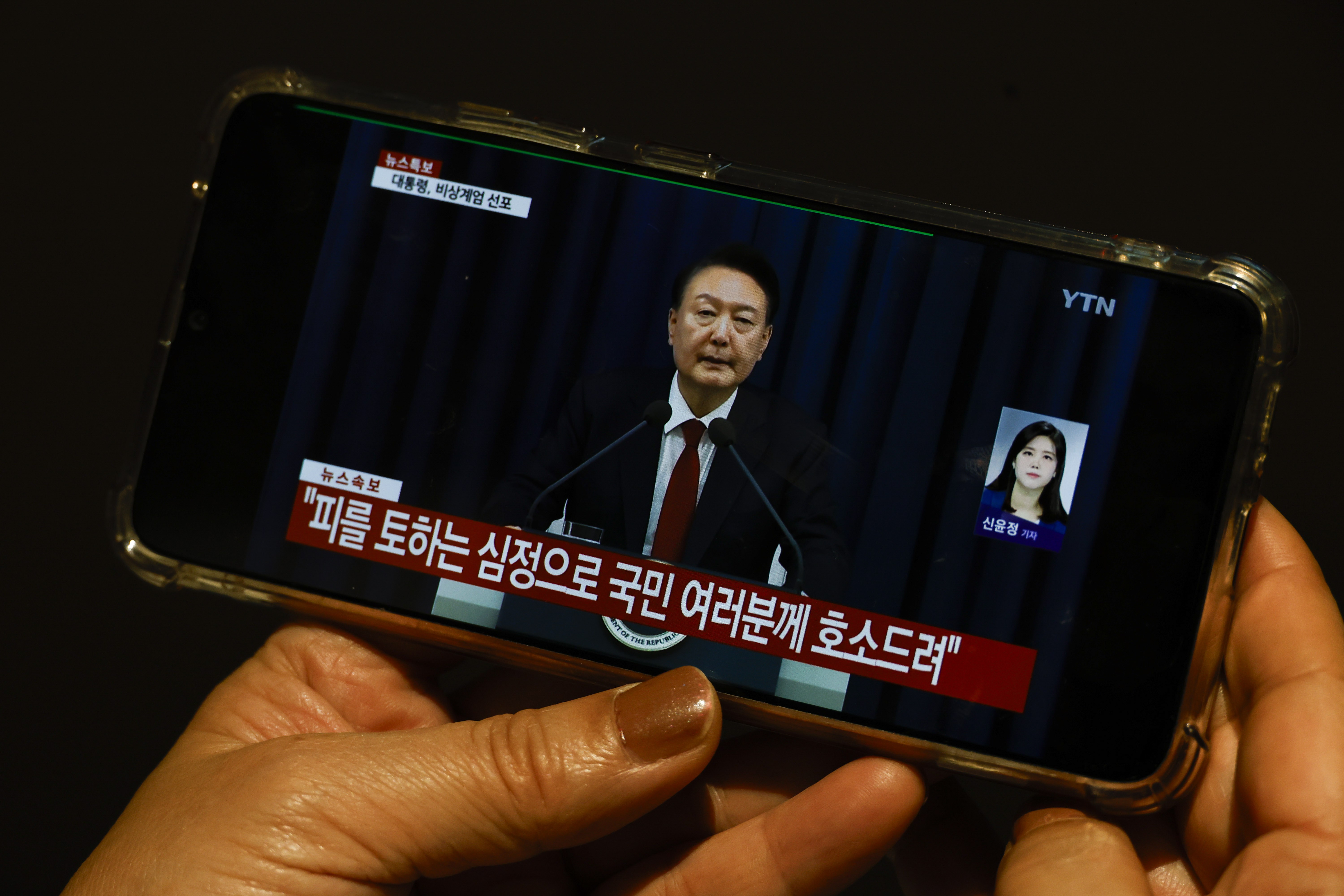 A South Korean tourist watches a Japanese TV broadcast on a phone showing South Korean President Yoon Suk Yeol