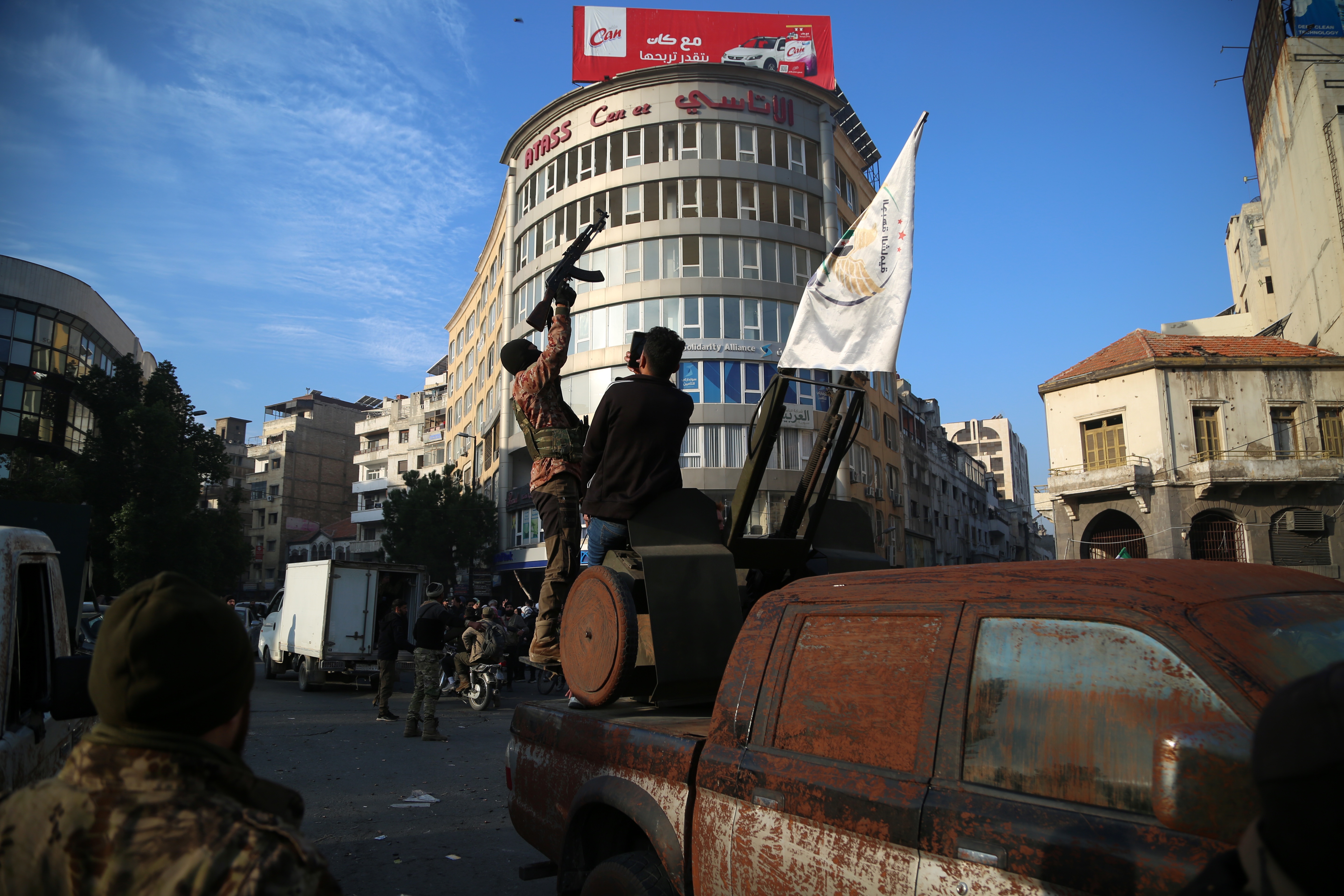 Syrian rebels ride on the back of a vehicle as people celebrate in the streets of Homs