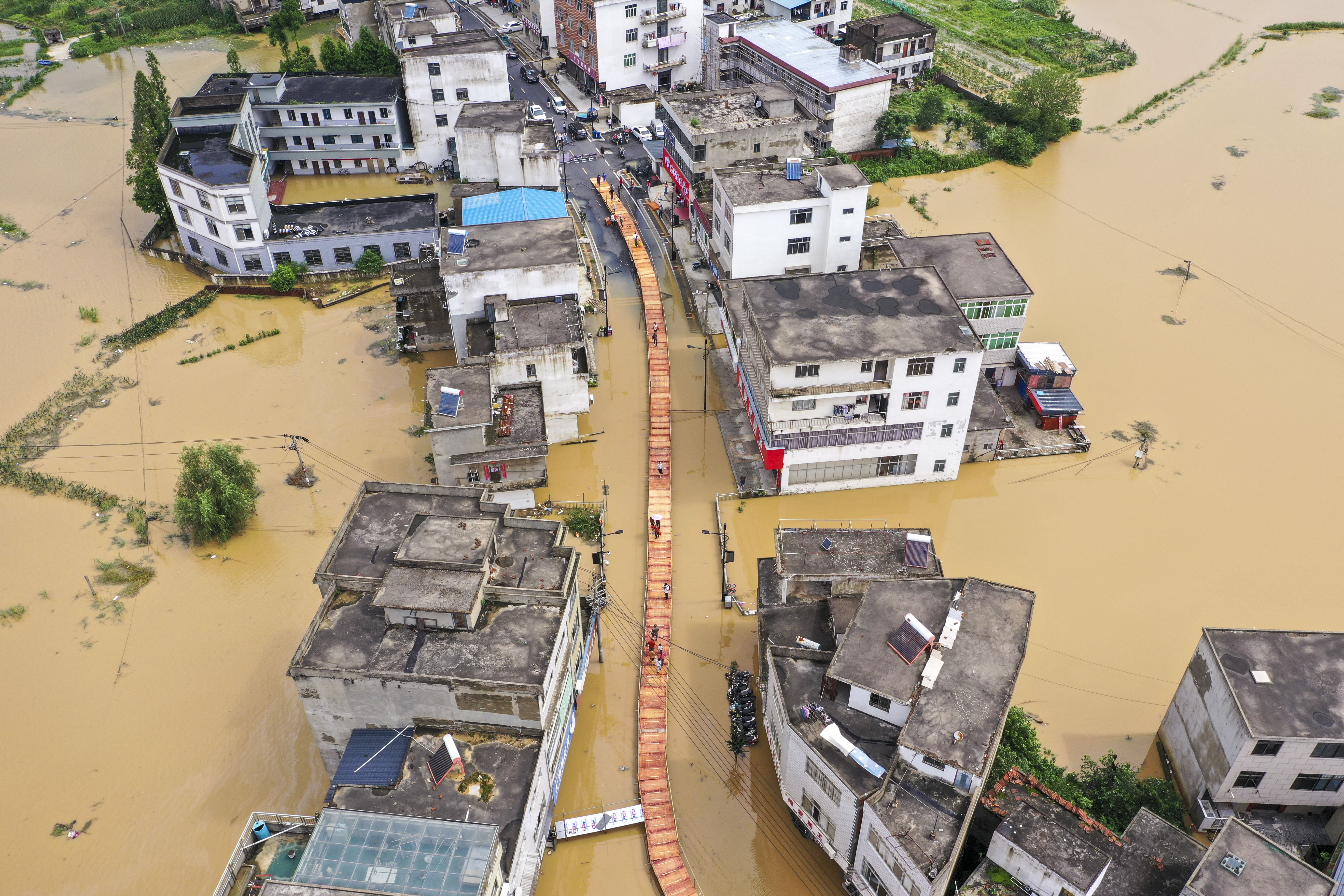 This photo shows an aerial view of people crossing a walkway built above flood waters on a street in Maying town in Jiujiang, in China's central Jiangxi province on July 3, 2024