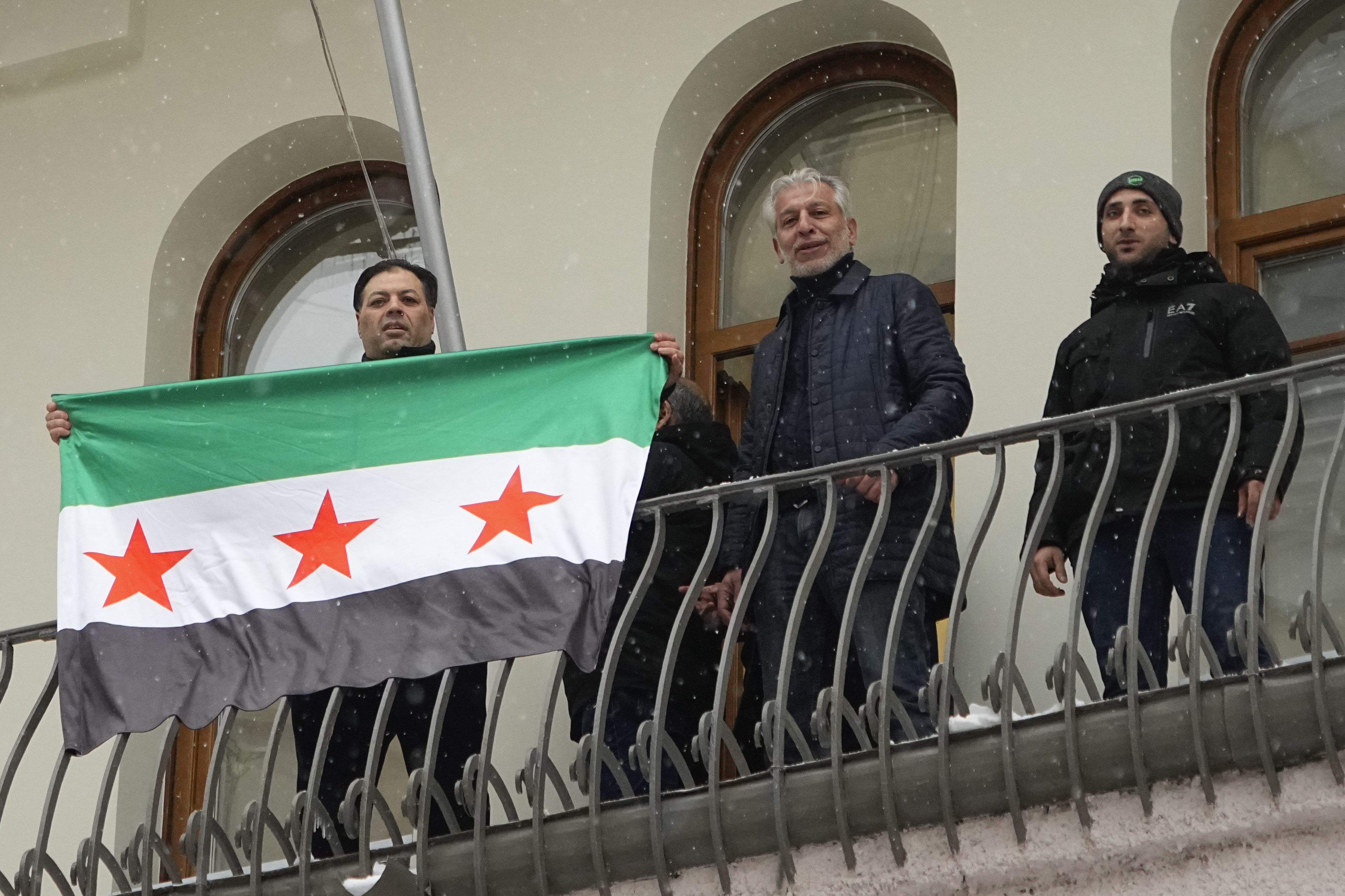 Members of the Syrian diaspora gesture while setting the Syrian opposition flag at the Syrian embassy, in Moscow