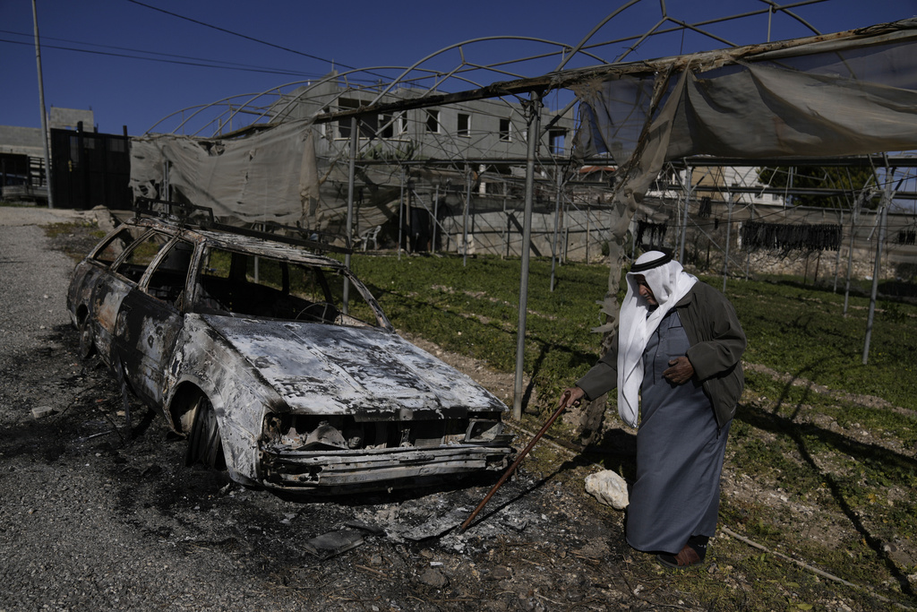 a man in grey robes stands next to a charred car