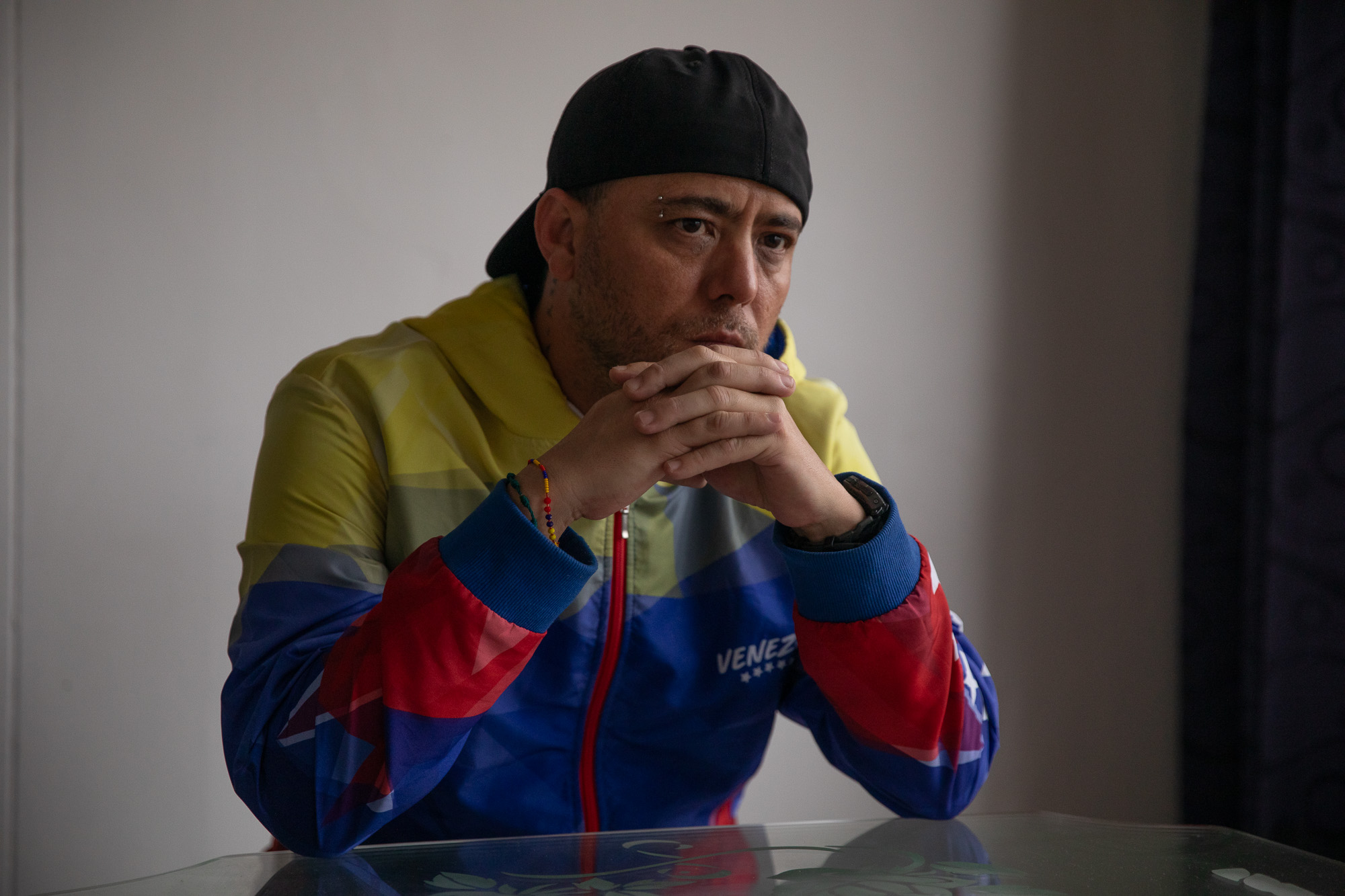 Jesus Medina, a Venezuelan photojournalist, leans against a table. He wears a coat patterned in the colors of the Venezuelan flag.
