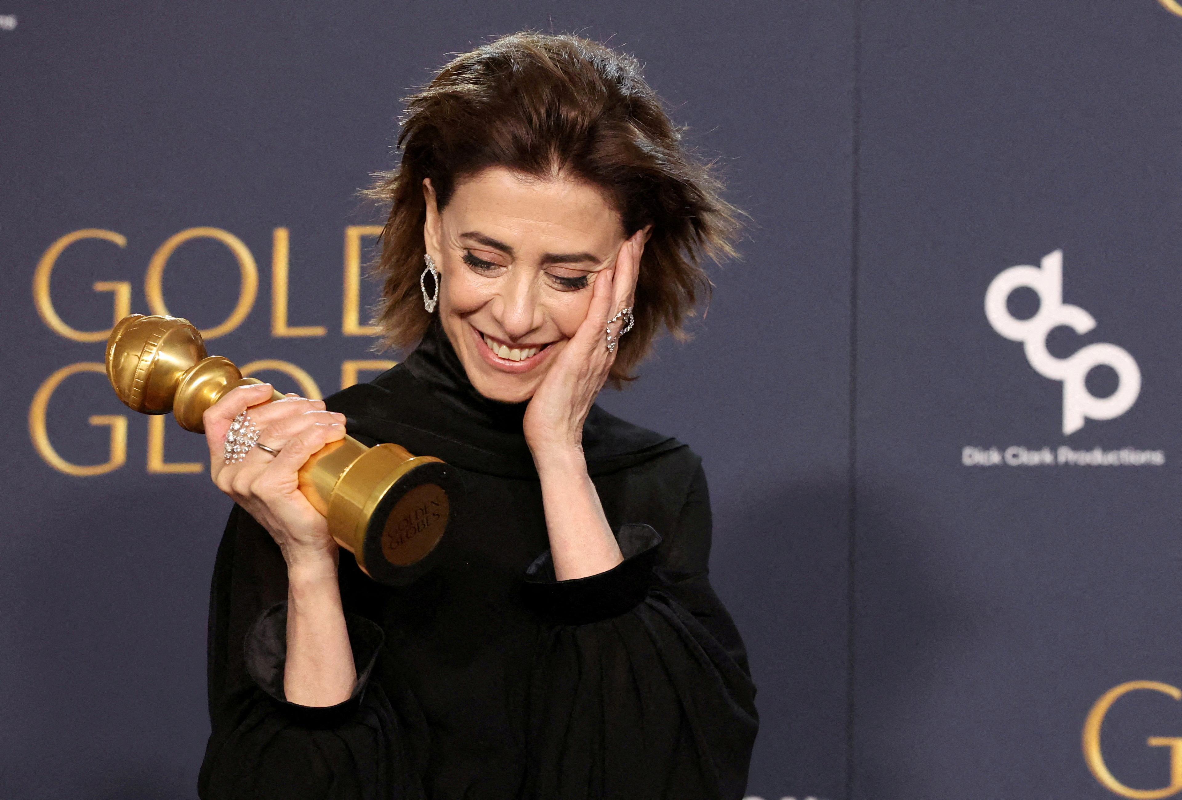 Fernanda Torres holds her Golden Globe on the red carpet, her hand on her face as she blushes