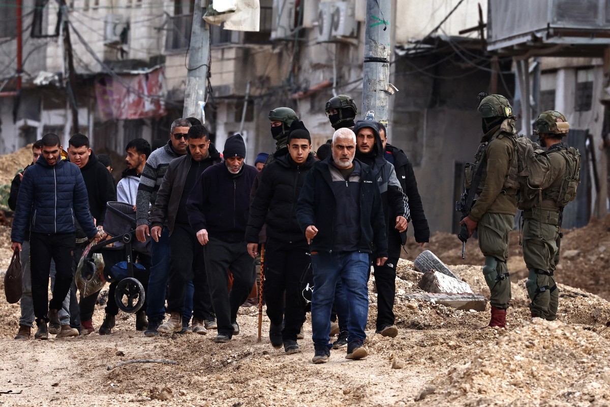 Israeli soldiers keep watch as Palestinians leave their homes for safety during a raid by the army in the Nur Shams refugee camp near Tulkarem in the occupied West Bank on February 10, 2025.