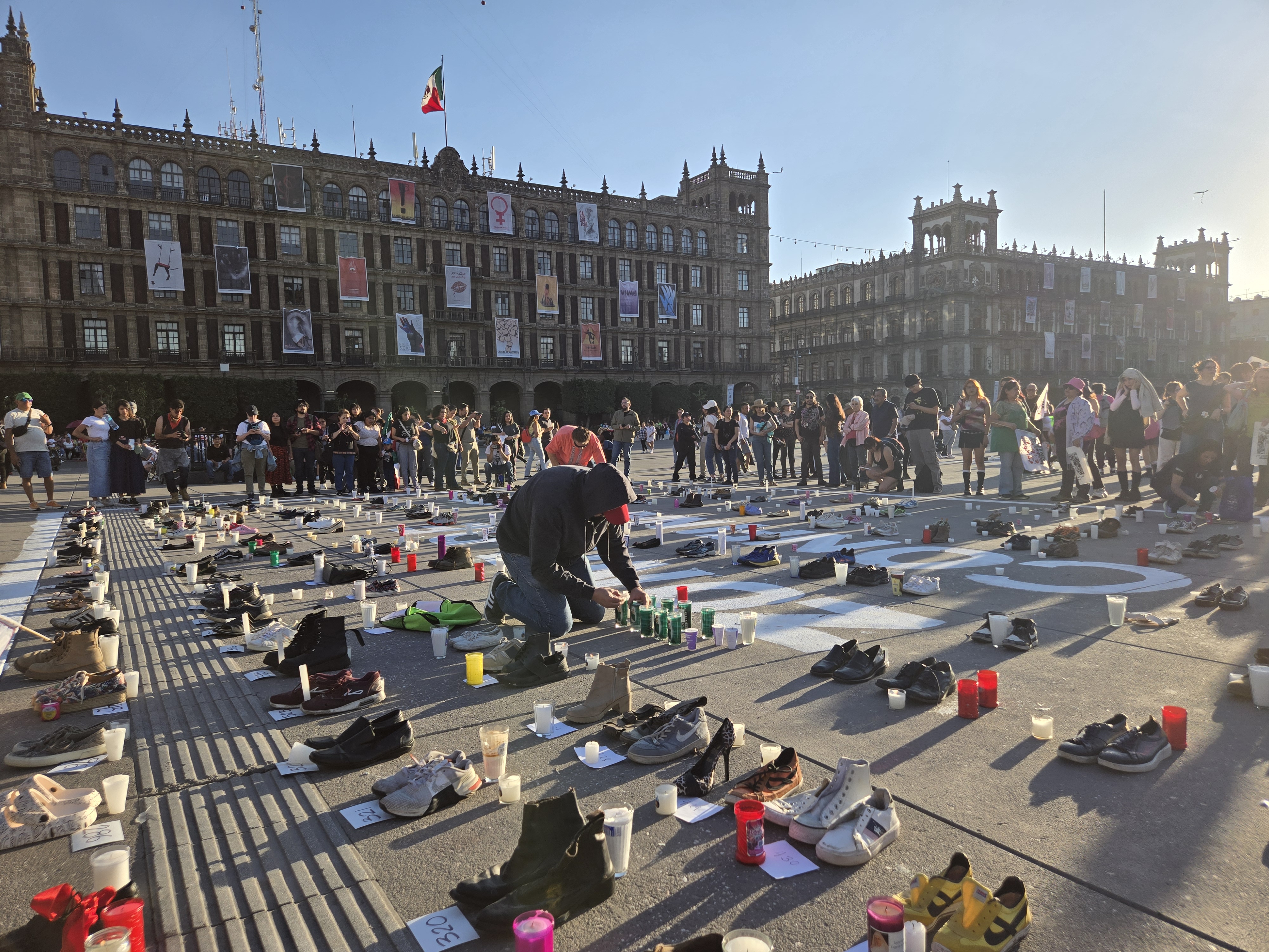 A protester lights candles next to shoes symbolizing Mexico's missing in the Zocalo plaza