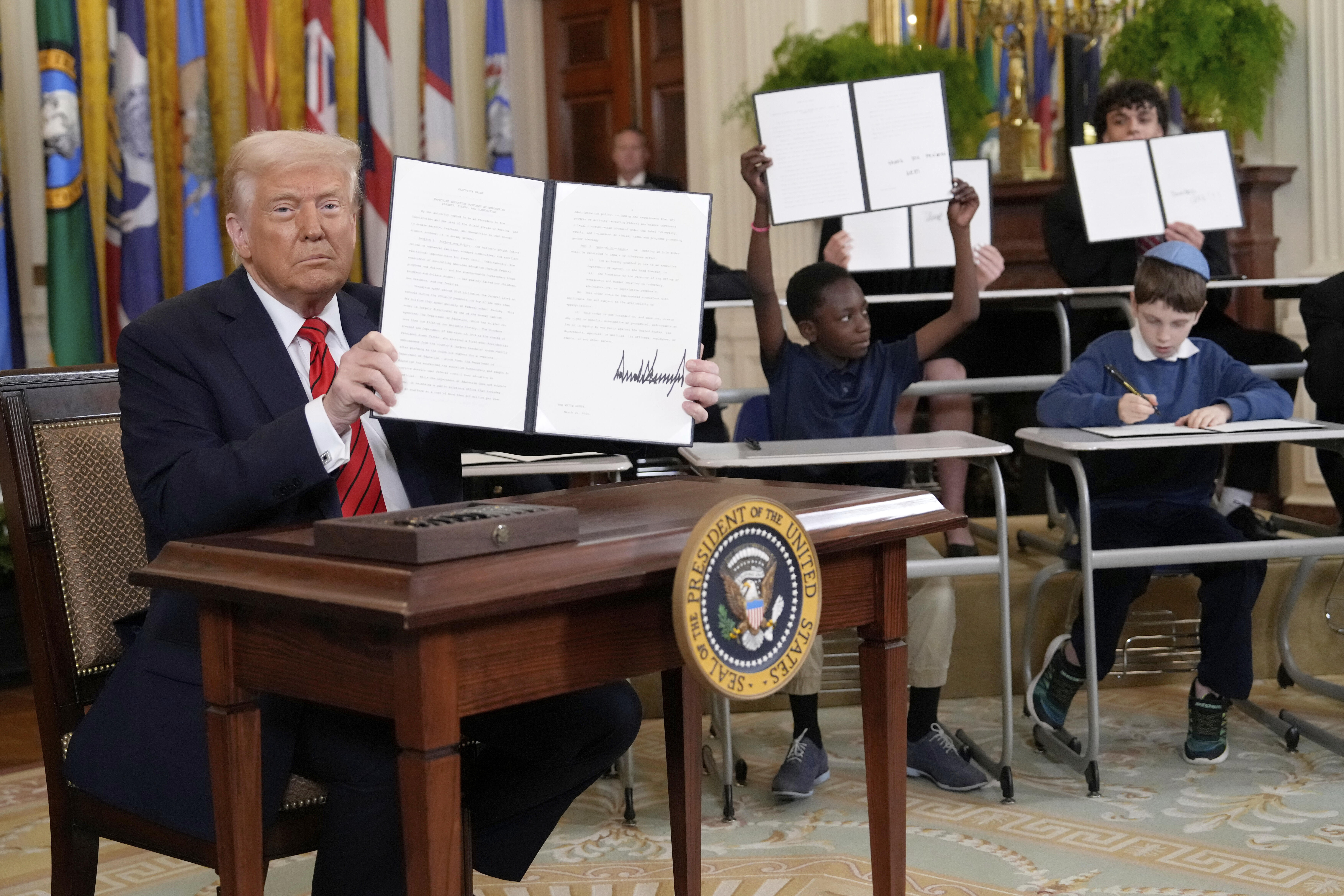 Donald Trump holds up his executive order, while kids do the same with their mock versions